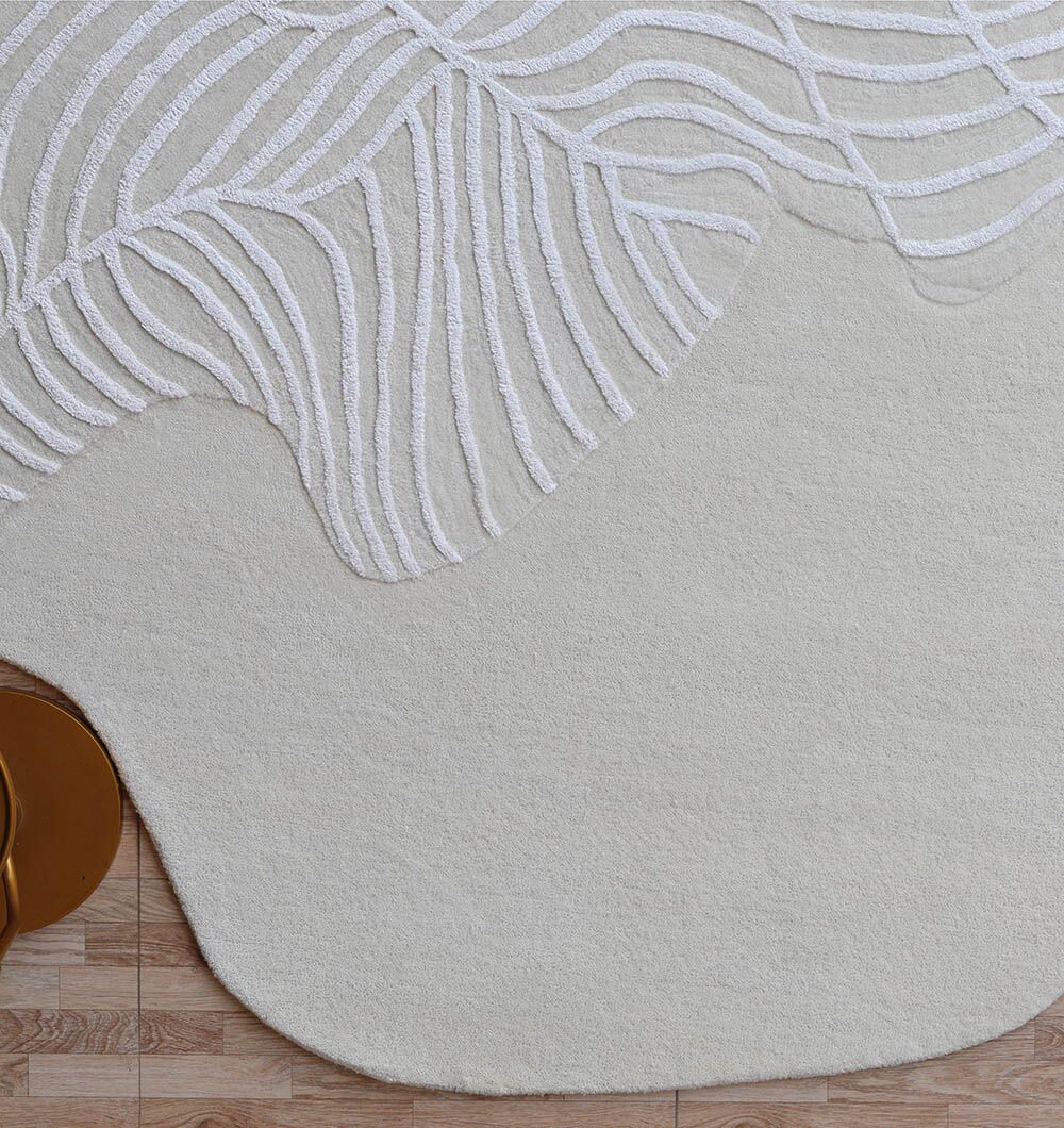The Off White Color Handmade Area Rug - HTWV-140 (200x300 cm) by RAMSHA HOME features wavy white lines in a leaf-inspired pattern on beige, shown on a light wooden floor with part of a round gold object at the lower left.
