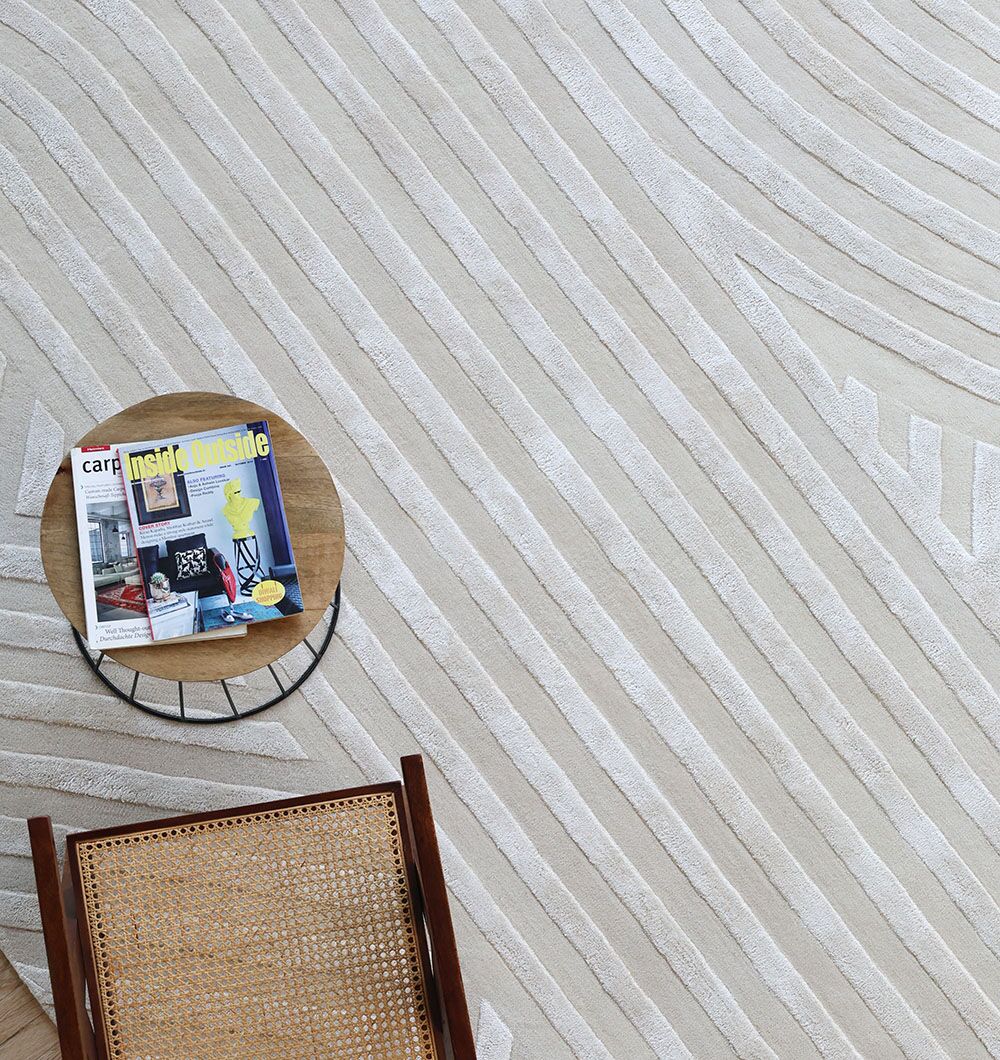 A round side table with magazines and a cane chair sit on the RAMSHA HOME Natural White Color Handmade Area Rug (HTWV-142, 300x400 cm), its light tone and textured patterns adding subtle elegance to the space.