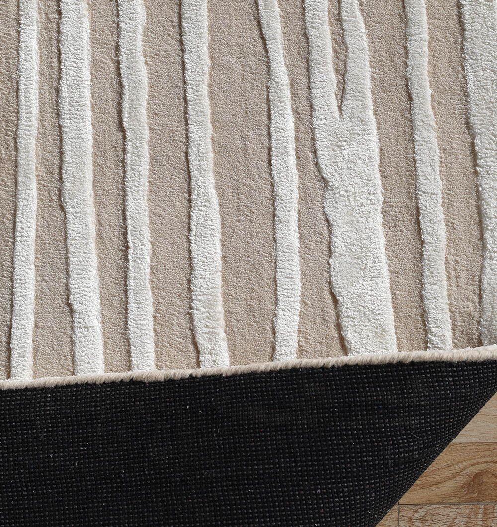 A close-up of the RAMSHA HOME Natural Color Handmade Area Rug (HTWV-147, 300x400 cm), featuring neutral stripes with raised white textures, slightly lifted to show its dark non-slip backing on a wooden floor.