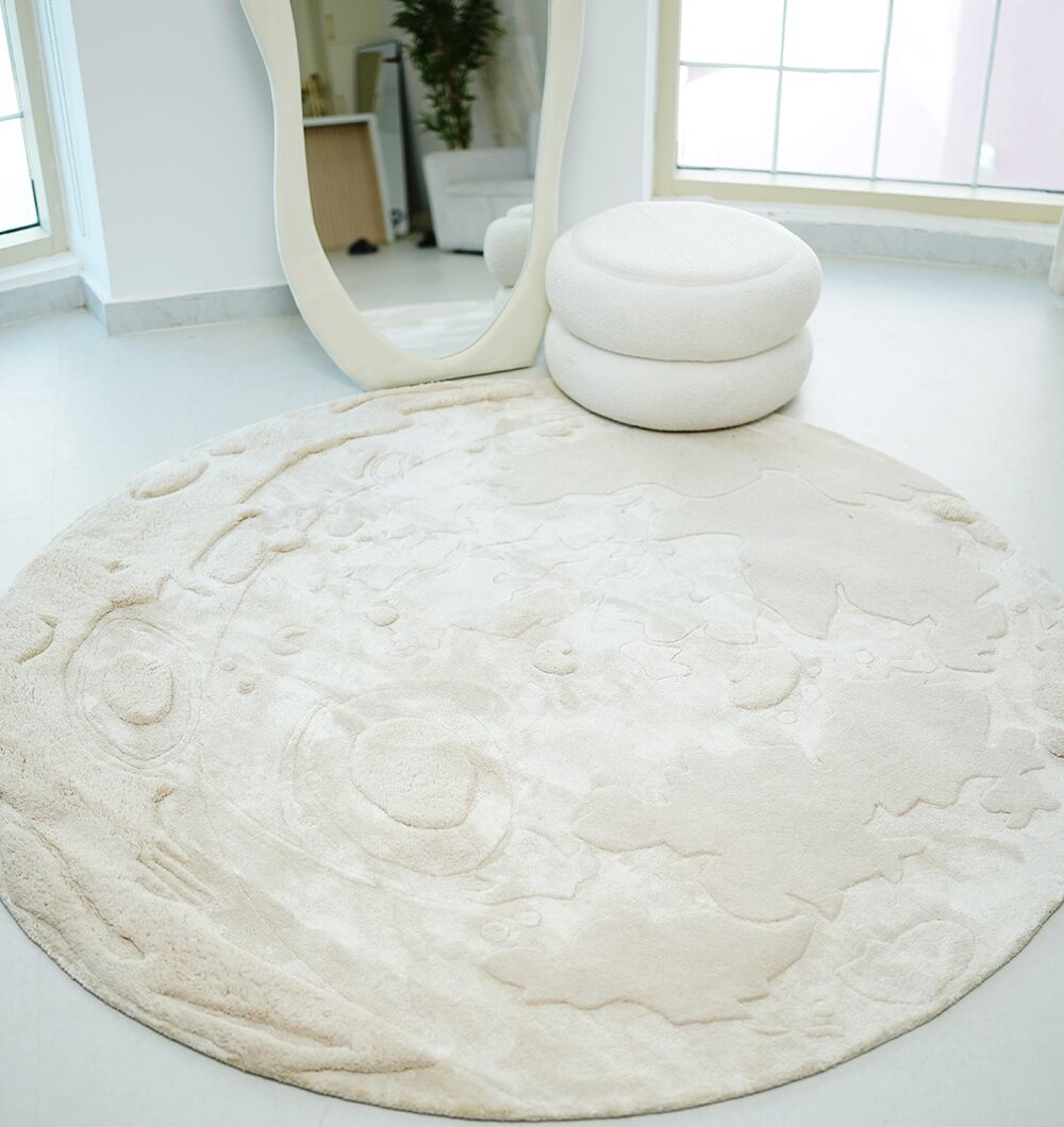 The RAMSHA HOME Natural Color Handmade Area Rug - HTWV-150 (200 cm) with moon-like textured patterns lies on a light floor, paired with a white round ottoman and large oval mirror for a serene, modern look.