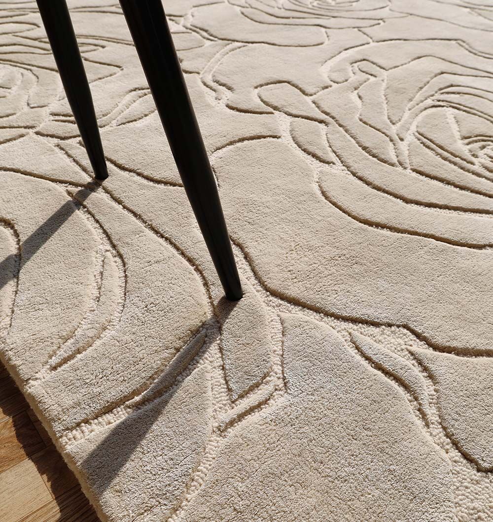 Close-up of the RAMSHA HOME Home Decor Handmade Area Rug - HTWV-156, featuring a beige floral design with a raised, carved texture. Detailed patterns and partial dark table or chair legs are visible on this hand-tufted wool rug.