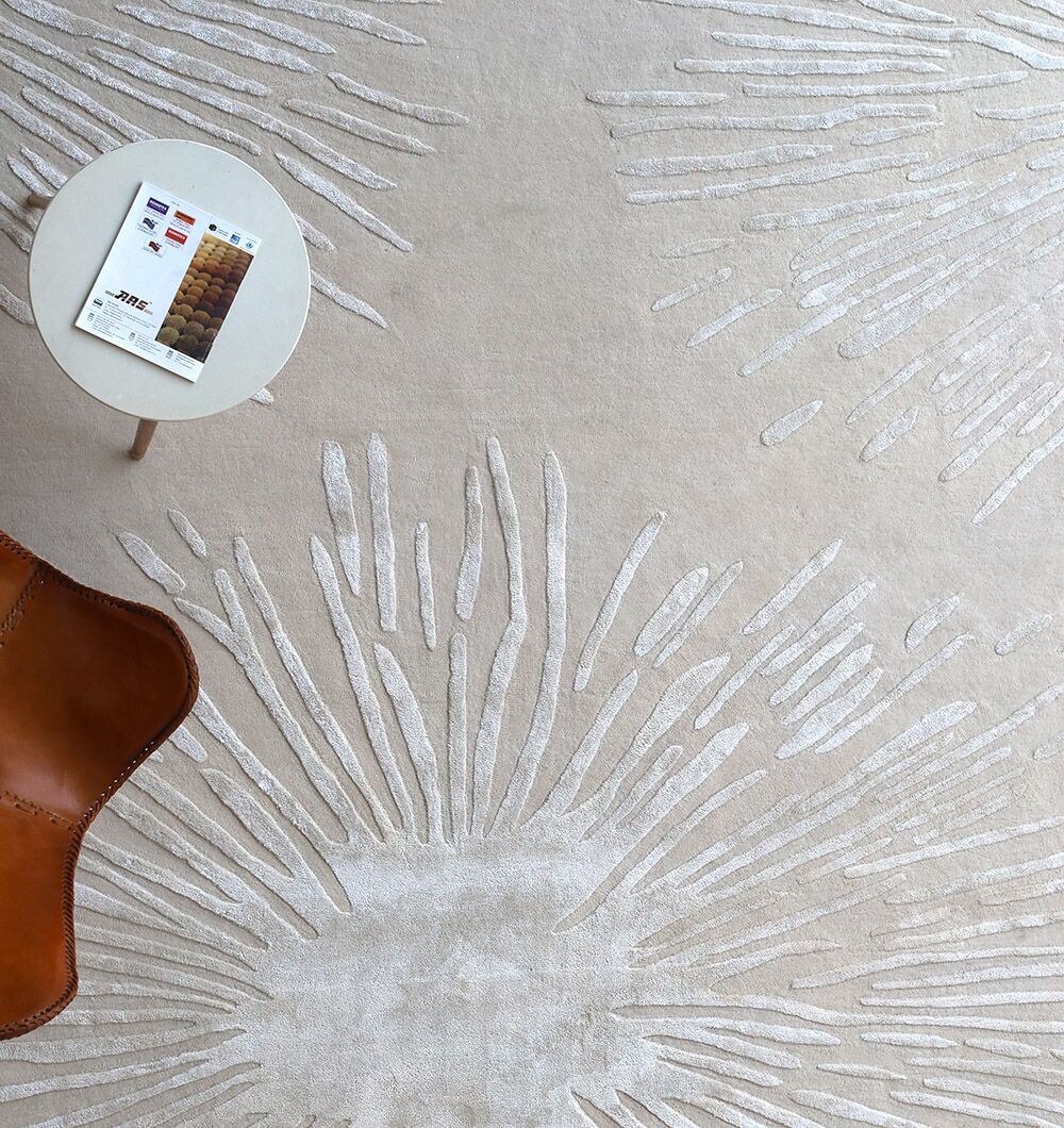 The RAMSHA HOME Rectangle Home Decor Light Beige Color Rug - HTWV 160 (300x400 cm) features a textured design, shown with a partial brown leather chair and a small round white side table holding a booklet.