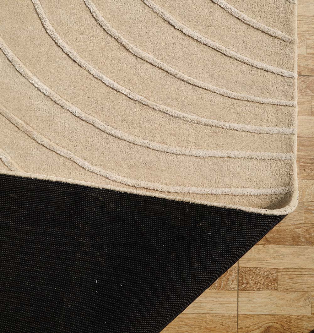 A Beige Color Handmade Decorative Area Rug - HTWV 161 (300X400 cm) by RAMSHA HOME with curved, raised lines is partially lifted to show a black rug pad beneath, both set on a light wood floor with a natural grain pattern.