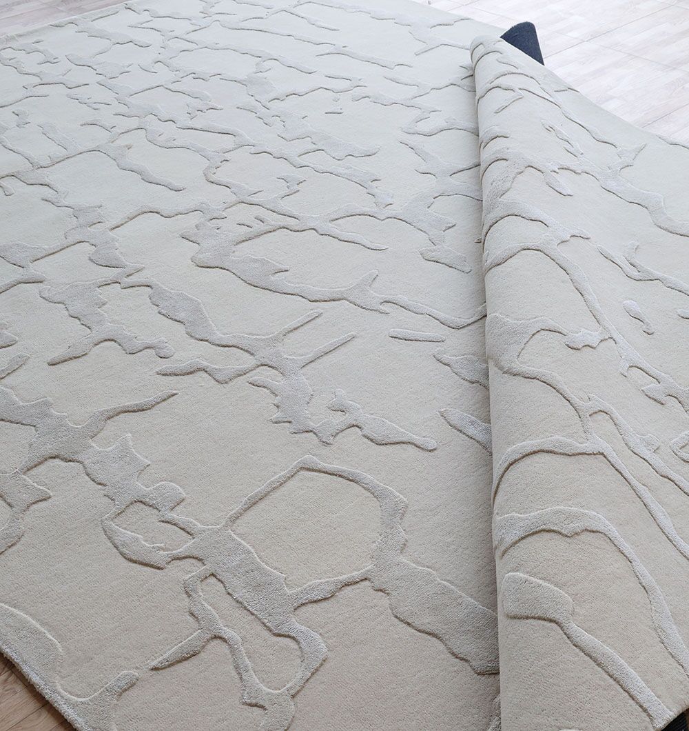 The RAMSHA HOME Handmade Textured Crackle Pattern Leather Rug - HTWV 163 (300x400 cm) is shown partially folded on a light wood floor, featuring an abstract raised design in shades of beige and cream.