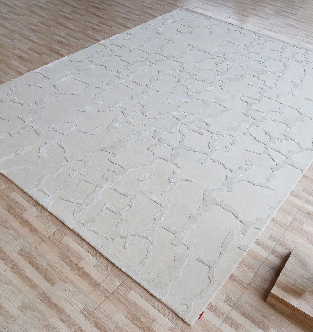 The RAMSHA HOME Handmade Textured Crackle Pattern Leather Rug - HTWV 163 (300x400 cm), in cream with raised abstract details, sits on a light wood-patterned floor in a brightly lit room.