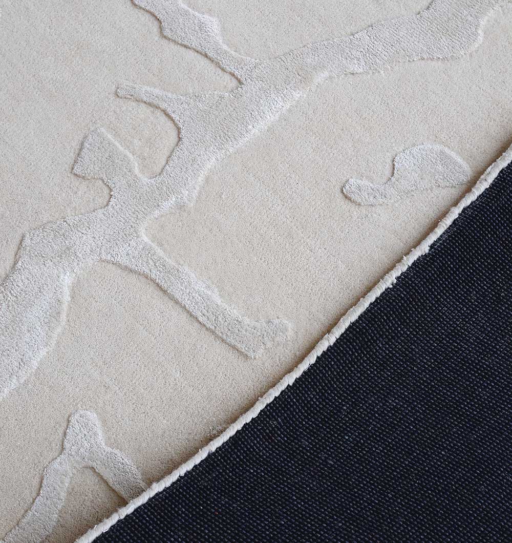A close-up of the RAMSHA HOME Handmade Textured Crackle Pattern Leather Rug - HTWV 163 (300X400 cm), cream-colored with a raised abstract design, shown partially folded to display its dark textured underside.