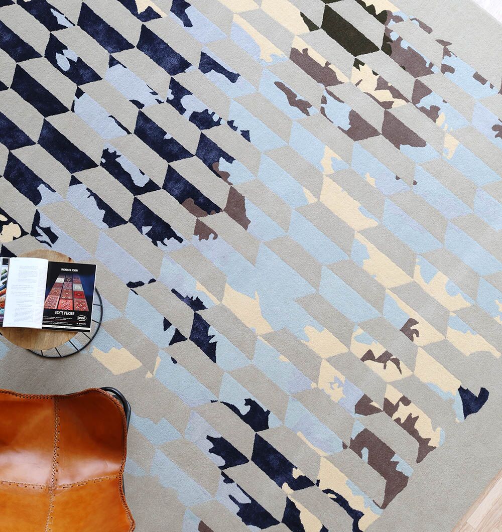 The RAMSHA HOME Multi Color Handmade Decorative Area Rug - HTWV 166 (300X400 cm) features modern geometric patterns in blue, beige, and gray. Style it with an open book and a brown leather ottoman for a chic look.