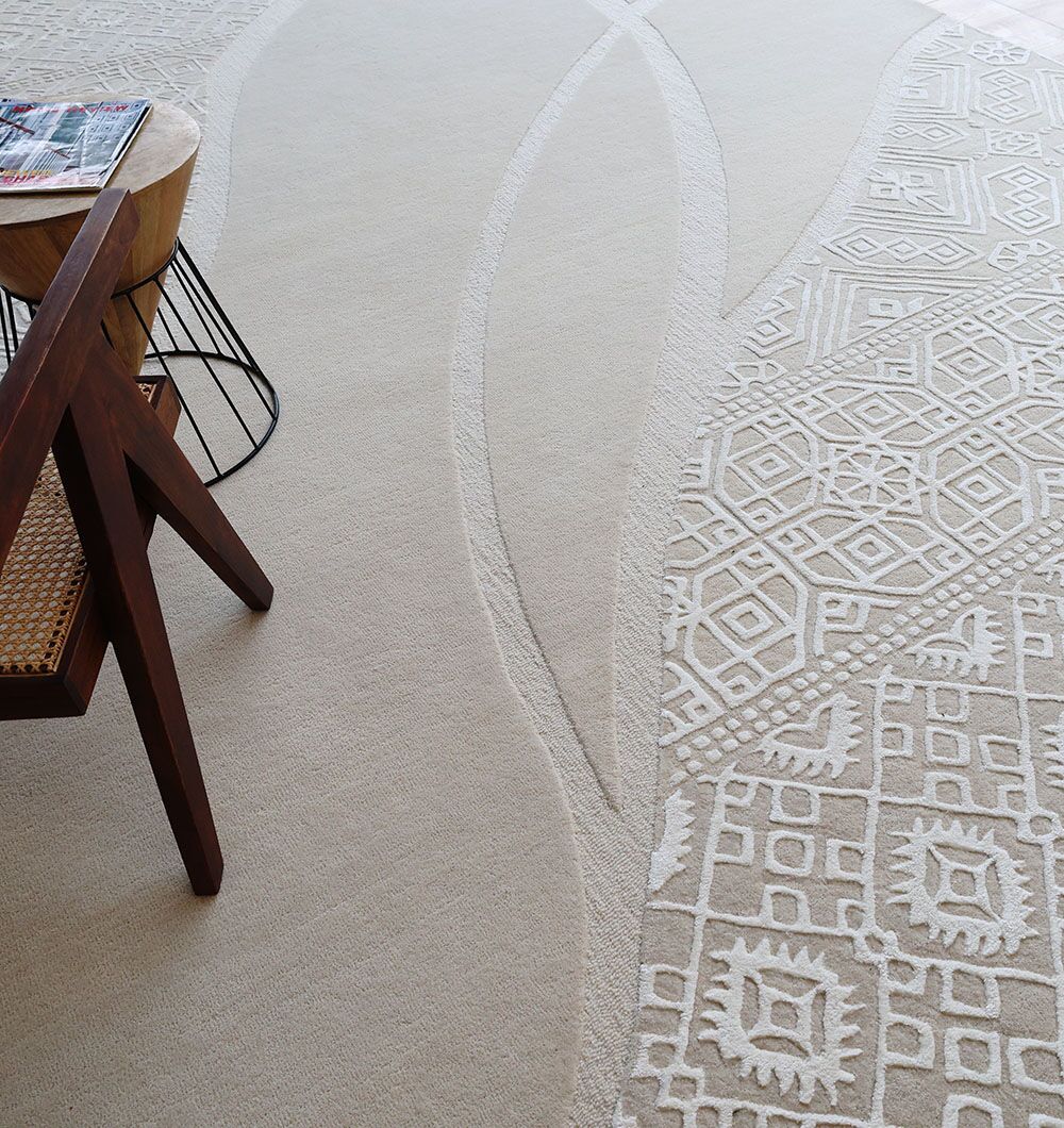 The RAMSHA HOME Boho Geometric Handmade Decorative Area Rug - HTWV 167 (300x400 cm) sits beside a wooden chair, a small round wooden side table, and a wire magazine holder topped with magazines.