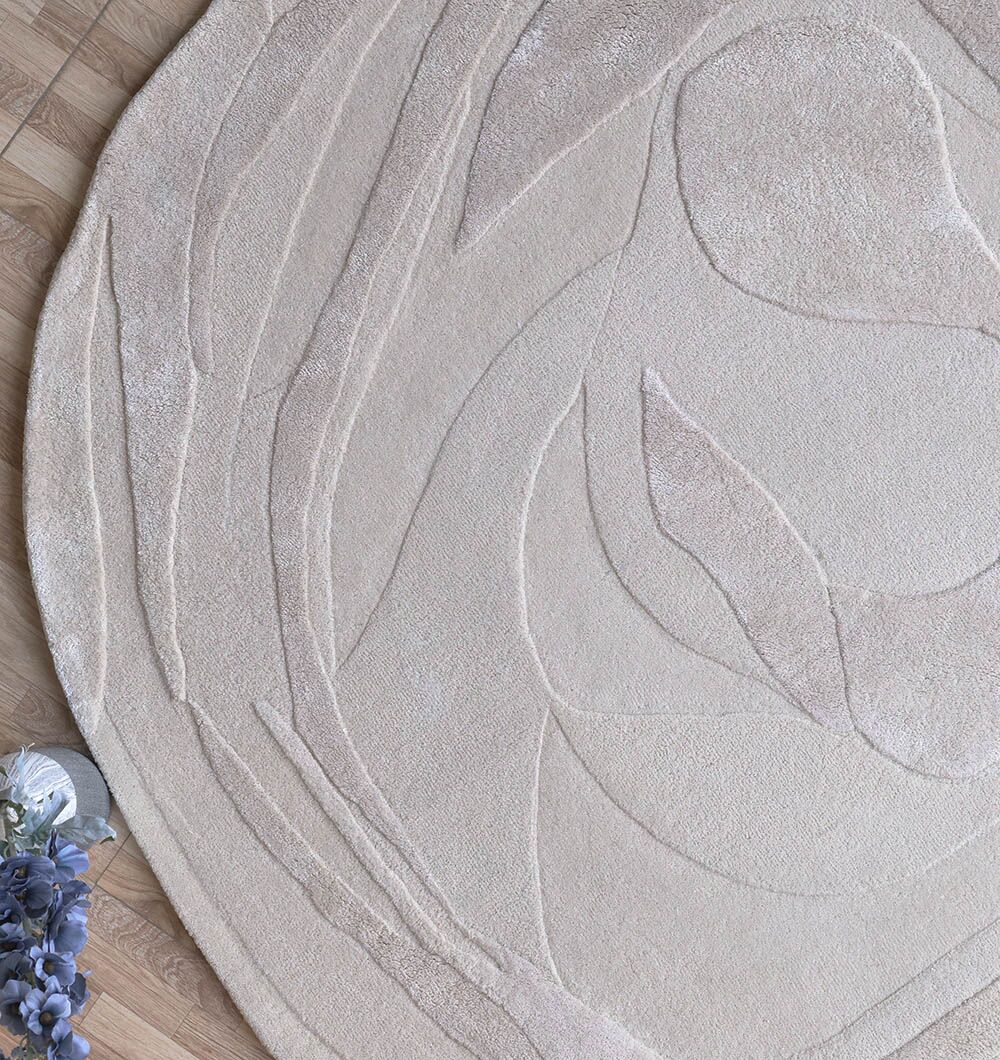 A close-up of the RAMSHA HOME Decorative Area Handmade Rug - HTWV 169 (200 cm) showcases its beige, abstract textured pattern on a wooden floor, with purple flowers in the corner adding charm to this modern scene.