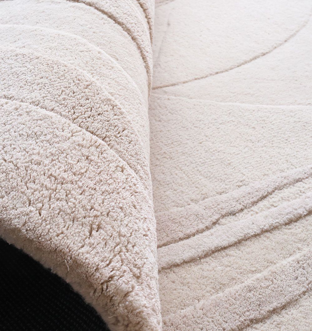 A close-up of the cream-colored RAMSHA HOME Decorative Area Handmade Rug - HTWV 169 (200 cm) shows its curved, raised patterns, with one corner lifted to reveal its black underside.