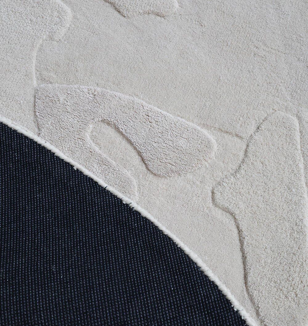 A close-up showcases the RAMSHA HOME Round Home Decor Handmade Rug - HTWV 170 (200 cm), featuring a cream abstract pattern and a curved section revealing its dark, woven underside—highlighting this stylish neutral rug.