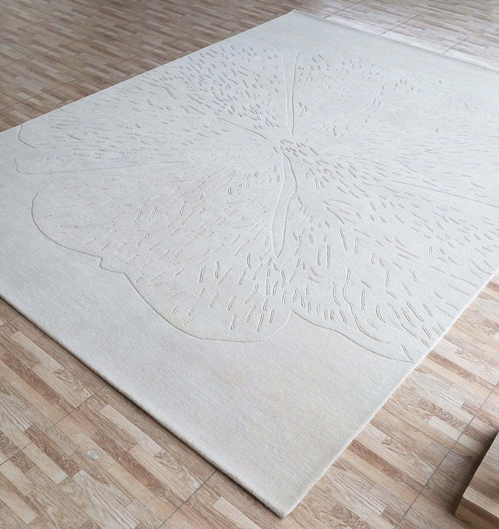 The RAMSHA HOME Embossed Floral Solid Light Grey Rug – HTWV 171, a large hand-tufted rug with subtle embossed floral patterns and soft, raised details, sits on a light wood-tiled floor and blends gently with its background.