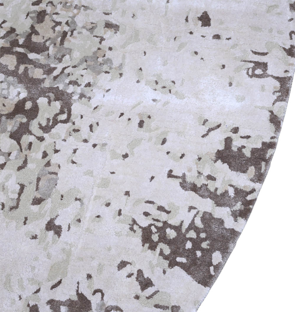 A close-up of the RAMSHA HOME Round Wool Handmade Carpet 350 cm (HTWV-173) showcases its abstract, camouflage-like pattern in neutral beige, brown, and off-white tones, with the round edge curving gracefully along the right side.