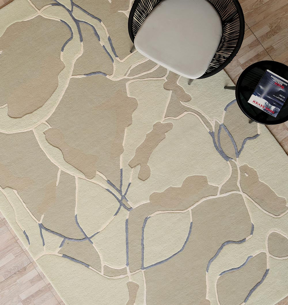 The Abstract Multi-Tone Handmade Carpet – HTWV-175 (200x300 cm) by RAMSHA HOME, featuring modern beige shapes and blue lines, lays on light wood flooring with a chic chair and black side table set on top.