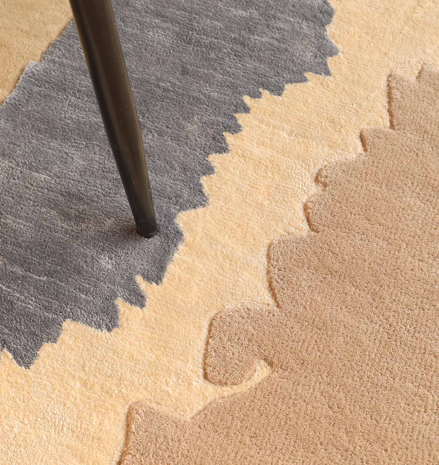 Close-up of the RAMSHA HOME Classic Rectangle Handmade Area Rug- HTWV 177 (300x400 cm) with beige, cream, and gray shapes. A black furniture leg stands on this hand-tufted viscose rug near the gray section's border.