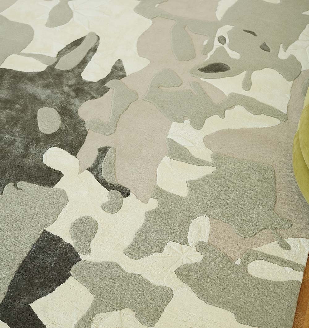 A close-up of the RAMSHA HOME Abstract Wool & Viscose Handmade Carpet 300x400 – HTWV-180 shows its beige, gray, cream, and olive green abstract pattern. A green piece of furniture appears at the right edge.
