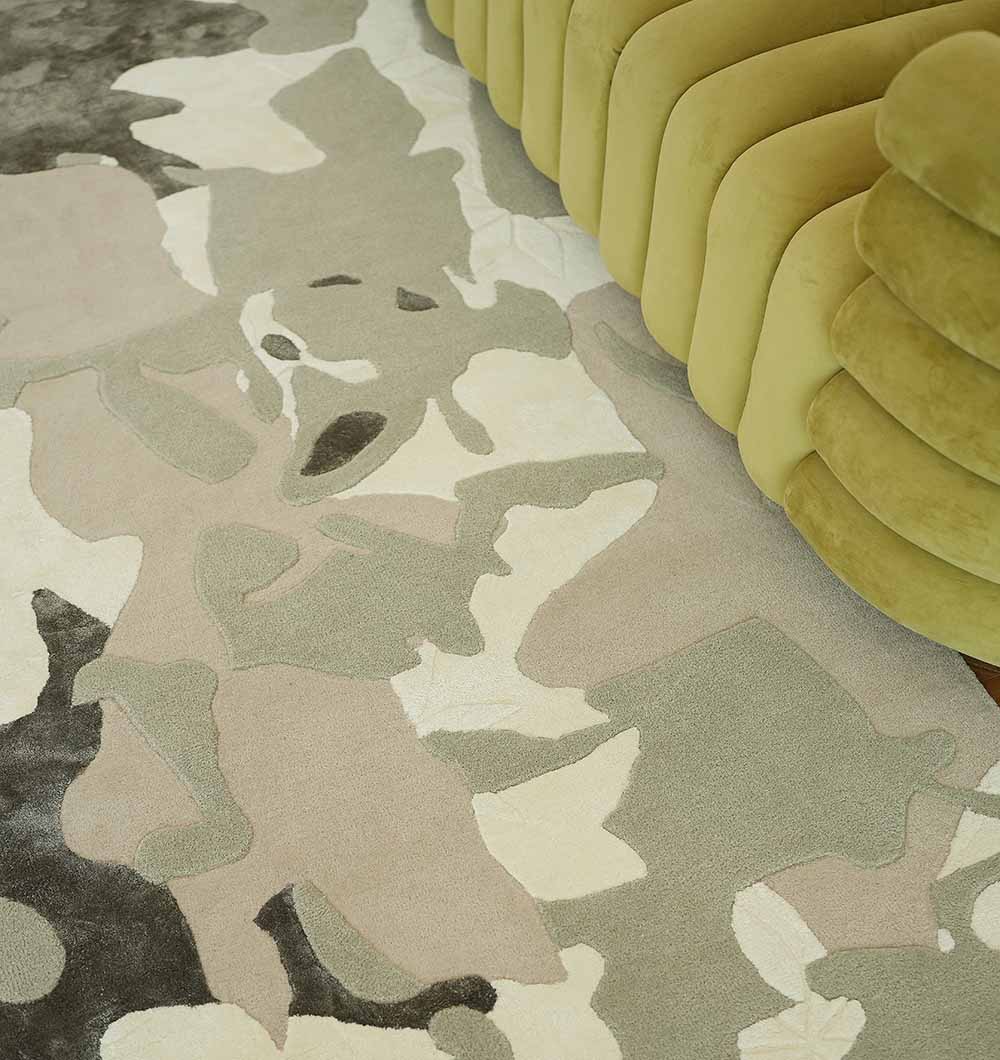 The RAMSHA HOME Abstract Wool & Viscose Handmade Carpet 300x400 – HTWV-180 features irregular, camouflage-style patterns in brown, beige, gray, and cream tones, shown beside a curved olive-green velvet sofa.