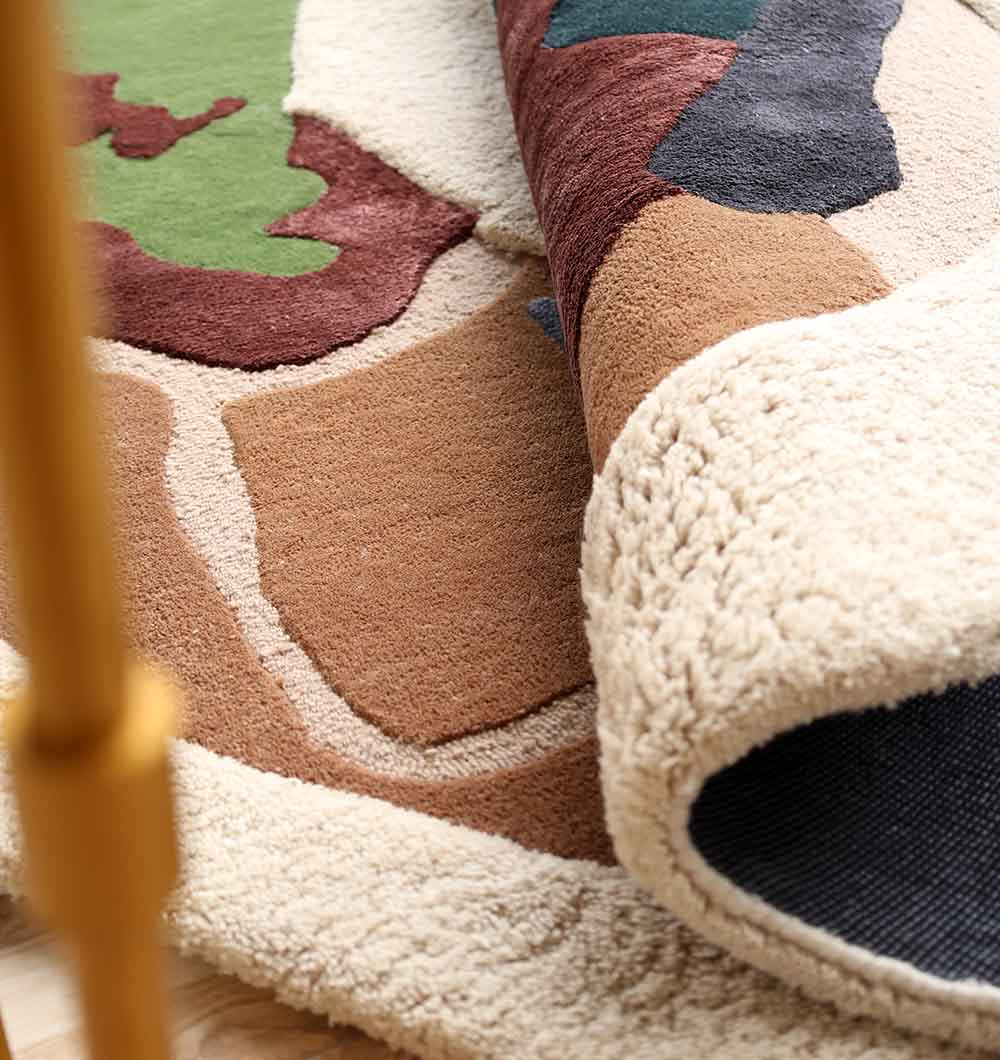 A close-up of the RAMSHA HOME Handmade Multicolor Abstract Shaped Rug HTWV 181 (200cm), partially rolled to display its thick, cream-colored underside and soft pile.