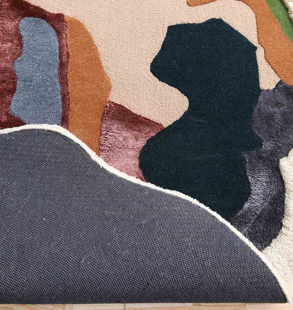 A close-up of the RAMSHA HOME Handmade Multicolor Abstract Shaped Rug HTWV 181 (200cm) shows curved black, brown, blue, tan, and green shapes with a flipped corner revealing its textured gray underside.