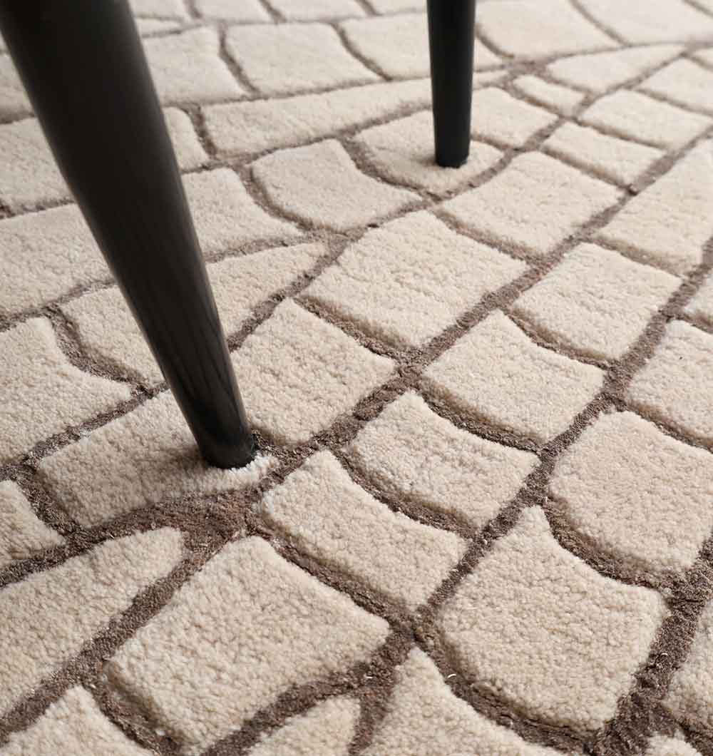 Close-up of the RAMSHA HOME Beige & Brown Decorative Handmade Shaped Rug HTWV 182 (200 cm), featuring a raised geometric cobblestone pattern in beige, with two dark chair legs resting on it.