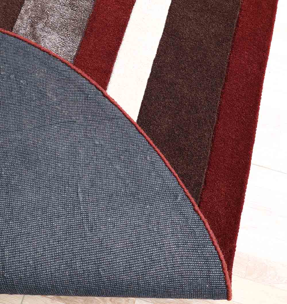 A corner of the RAMSHA HOME Modern Geometric Shaped Rug HTWV 184 (200 x 226 cm) is flipped to reveal its gray textured underside. The abstract wool rug has red, brown, and cream stripes on a light wooden floor.