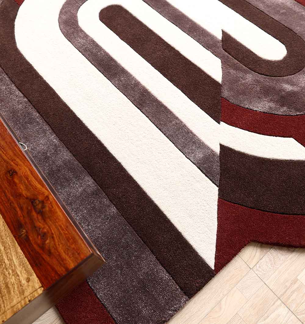 The RAMSHA HOME Modern Geometric Shaped Rug HTWV 184 (200 x 226 cm) features curved patterns in white, brown, maroon, and gray tones and is shown beside a wooden table on a light-colored floor.