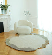 A cozy, rounded white armchair rests on the RAMSHA HOME Decorative Handmade Modern Shaped Rug HTWV 185 (183 x 200 cm) in a bright room with wood floors, a white fireplace, and large windows with sheer curtains.