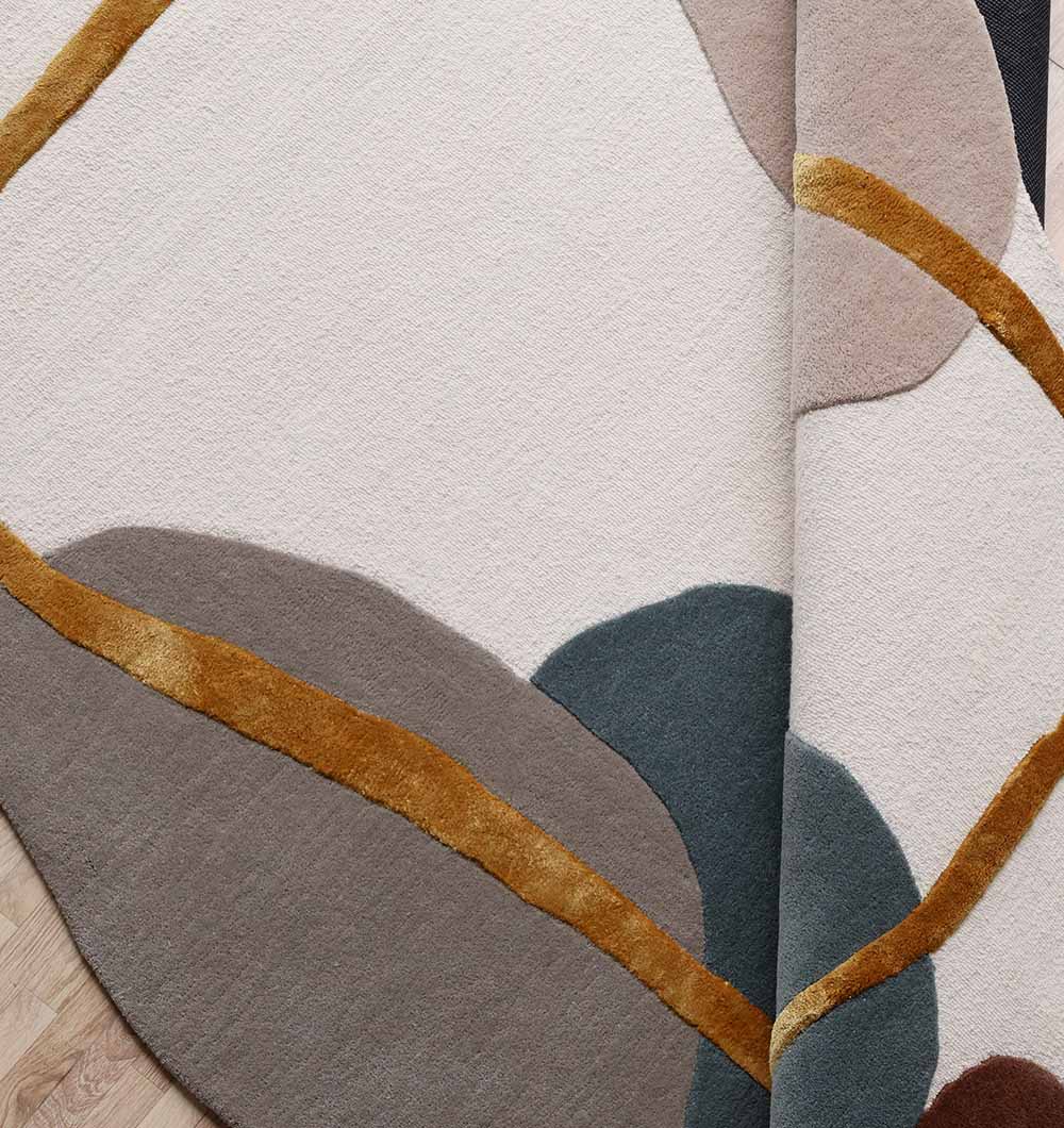 The RAMSHA HOME Handmade Multi Color Shaped Area Rug 200x300 CM HTWV 186 features abstract curved shapes in gray, cream, beige, mustard yellow, and dark green with overlapping geometric patterns. A folded corner reveals detail on a wooden floor.