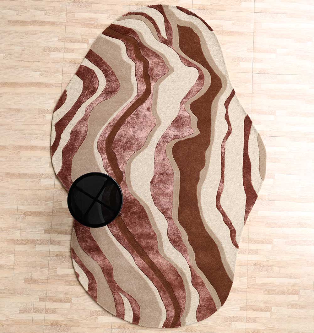 The Decorative Handmade Multi Color Shaped Area Rug – HTWV 187 by RAMSHA HOME, featuring abstract brown, beige, and cream stripes in an irregular design, lies on a light wooden floor partially under a round black side table.