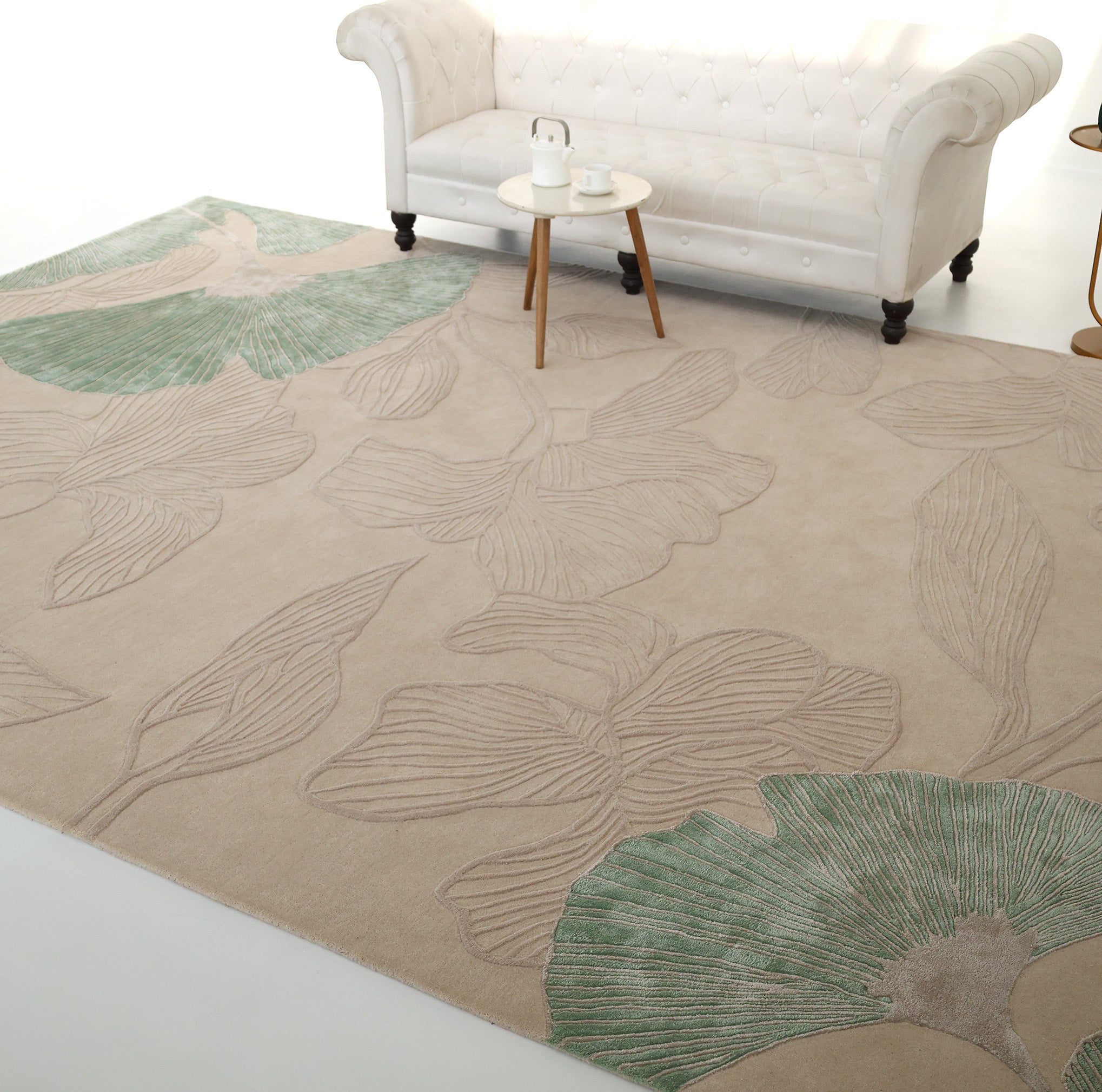 The RAMSHA HOME Floral Handmade Rectangle Rug HTWV-189 in beige, with green and taupe leaf patterns, is placed under a white tufted sofa and a small round table set with a teapot and cups.
