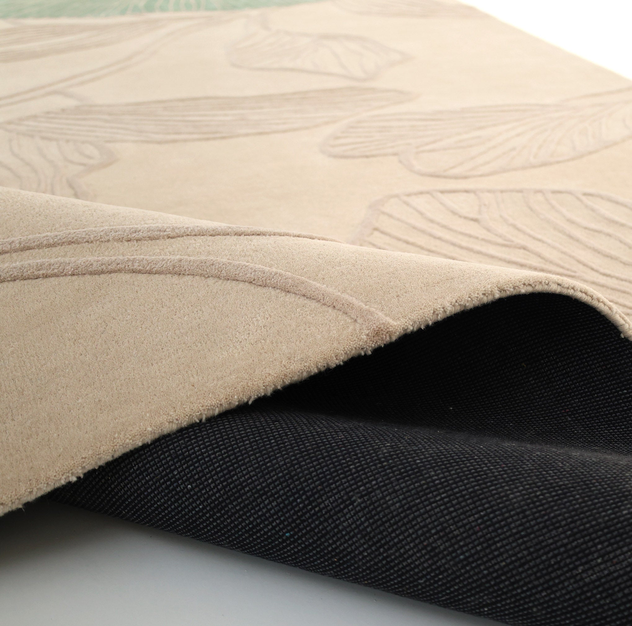 A close-up of the RAMSHA HOME Floral Handmade Rectangle Rug HTWV-189 in beige, featuring a raised leaf pattern and partially lifted to show its black non-slip backing.