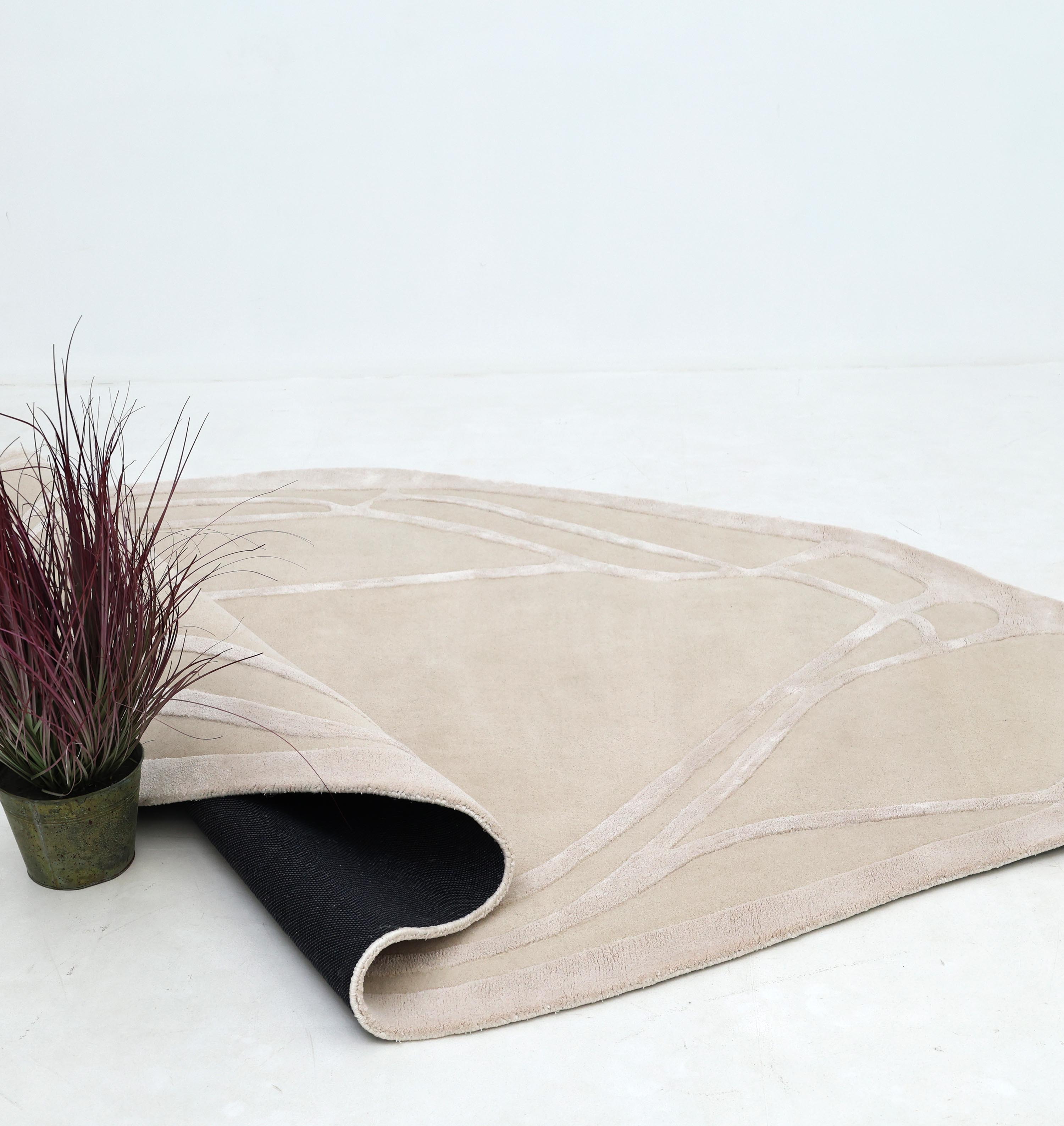 The RAMSHA HOME Handmade irregular 200x300 cm Rug HTWV-190 features abstract cream and beige lines and a black underside. Shown partially flipped, it sits on a white floor beside a potted plant with purple-green leaves against a plain background.