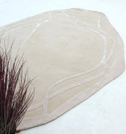 The RAMSHA HOME Handmade irregular 200x300 cm Rug HTWV-190 features beige tones and subtle abstract lines on a light floor, with dried decorative grass with reddish-purple stems shown in the lower left corner.
