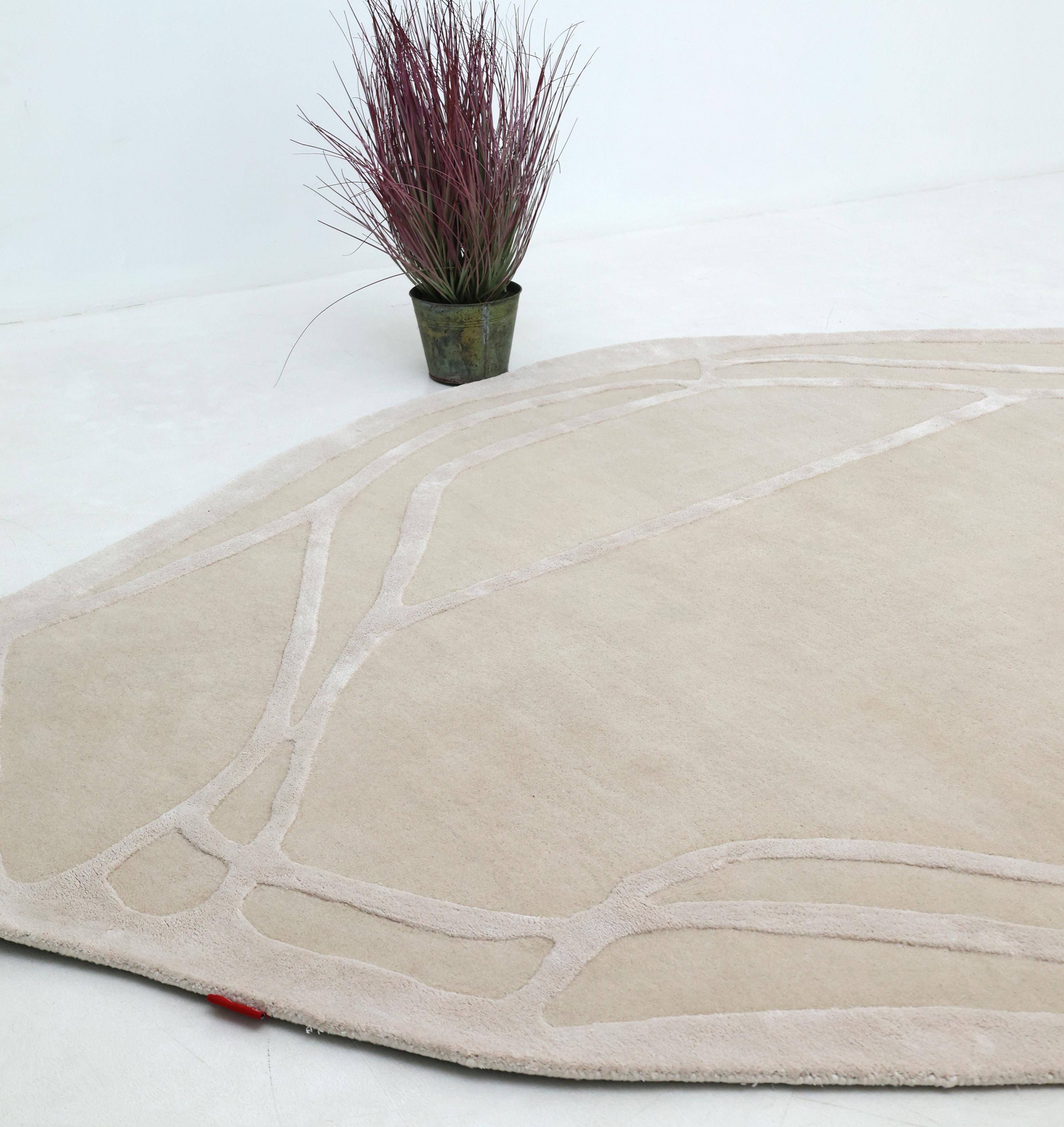 The RAMSHA HOME Handmade irregular 200x300 cm Rug HTWV-190, in cream and beige with abstract lines, lies on a light floor near a potted plant with tall purple-brown foliage against a white wall.