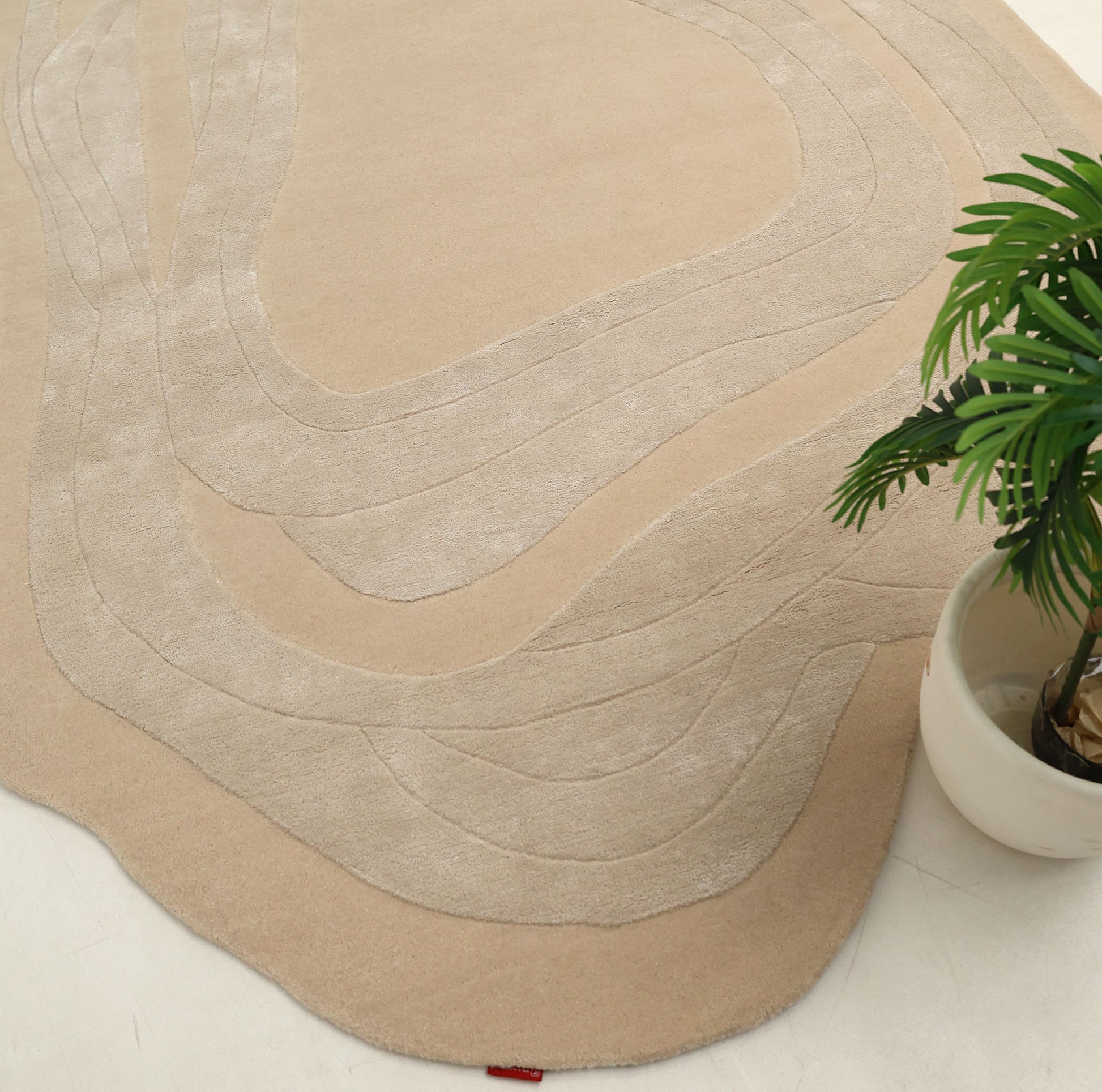 The RAMSHA HOME Handmade irregular 200x300 cm Rug HTWV-191, featuring cream and beige geometric patterns, is placed on a light floor beside a green potted plant in a white planter.