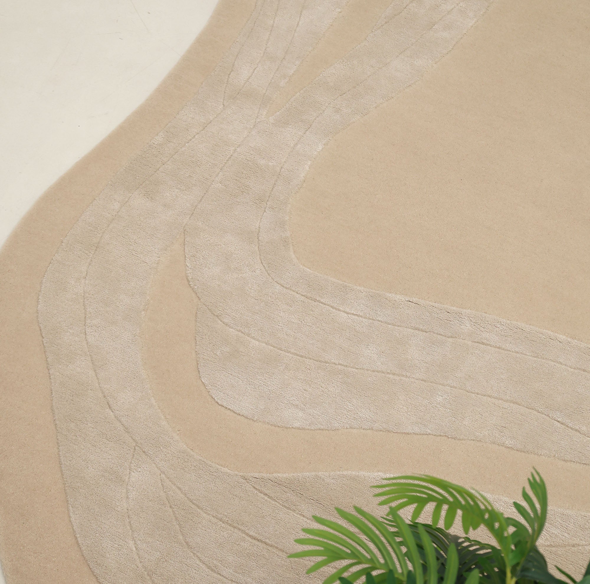 The RAMSHA HOME Handmade irregular 200x300 cm Rug HTWV-191 features cream and beige geometric curved line patterns on a light floor, with a small green plant partly seen in the lower right corner.