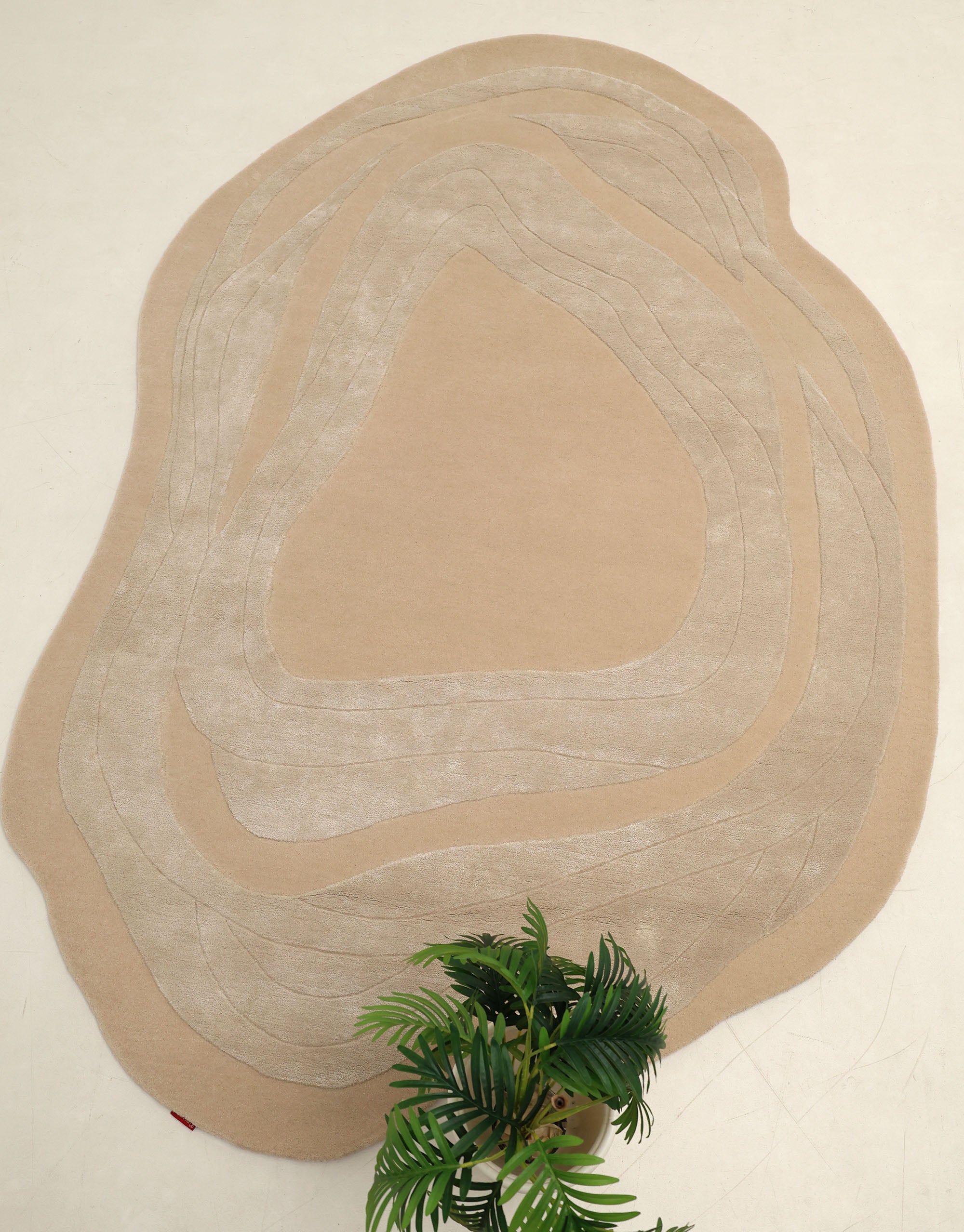 The RAMSHA HOME Handmade irregular 200x300 cm Rug HTWV-191, featuring cream and beige geometric patterns, is displayed on a light floor. A green artificial plant appears partially at the bottom of the image.