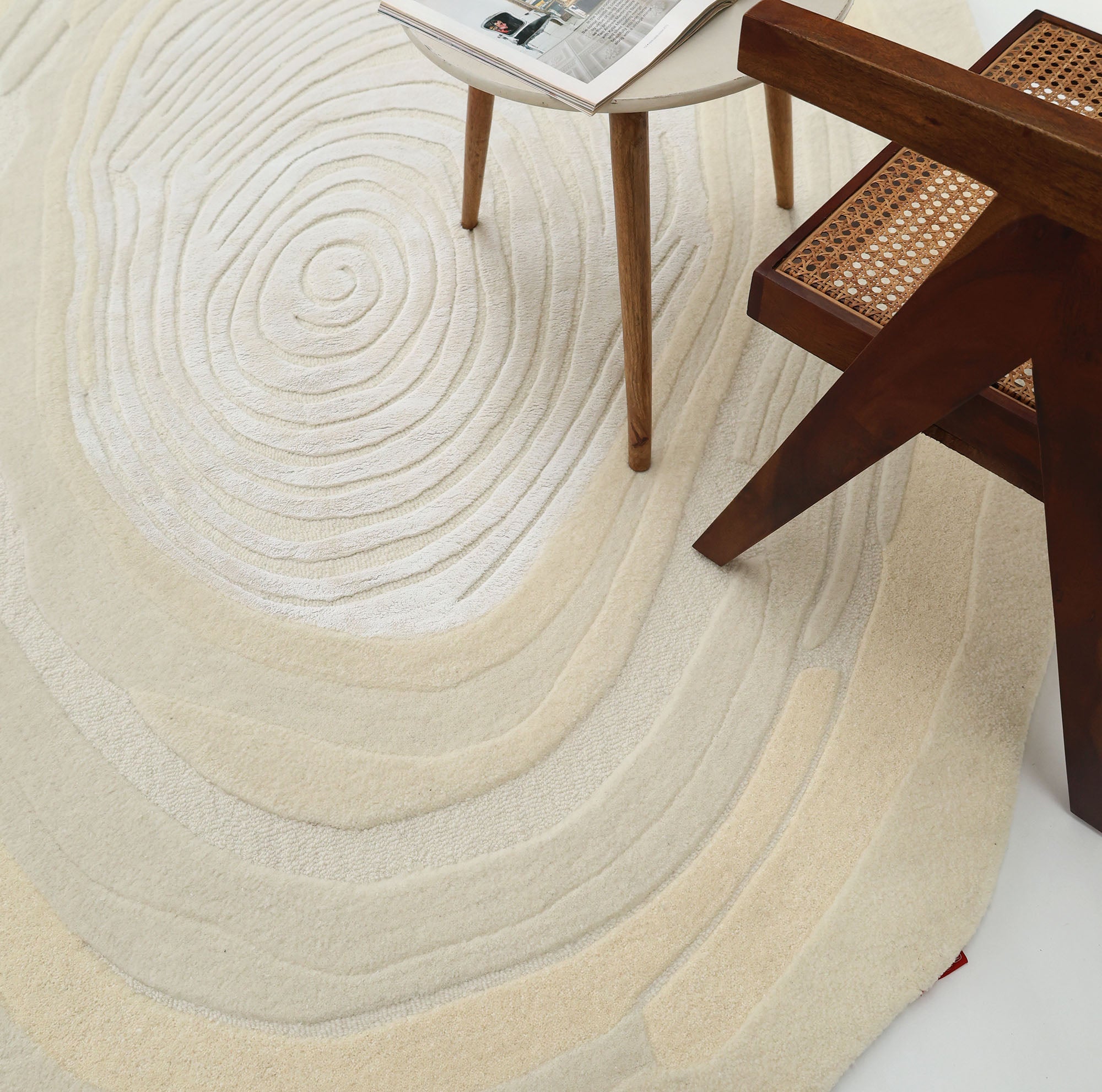 The RAMSHA HOME Ivory Topographic Shaped Rug 200x300 cm (Rug HTWV-192) features beige and cream circular, layered patterns, shown beneath a wooden chair and table, adding texture and style to any room.