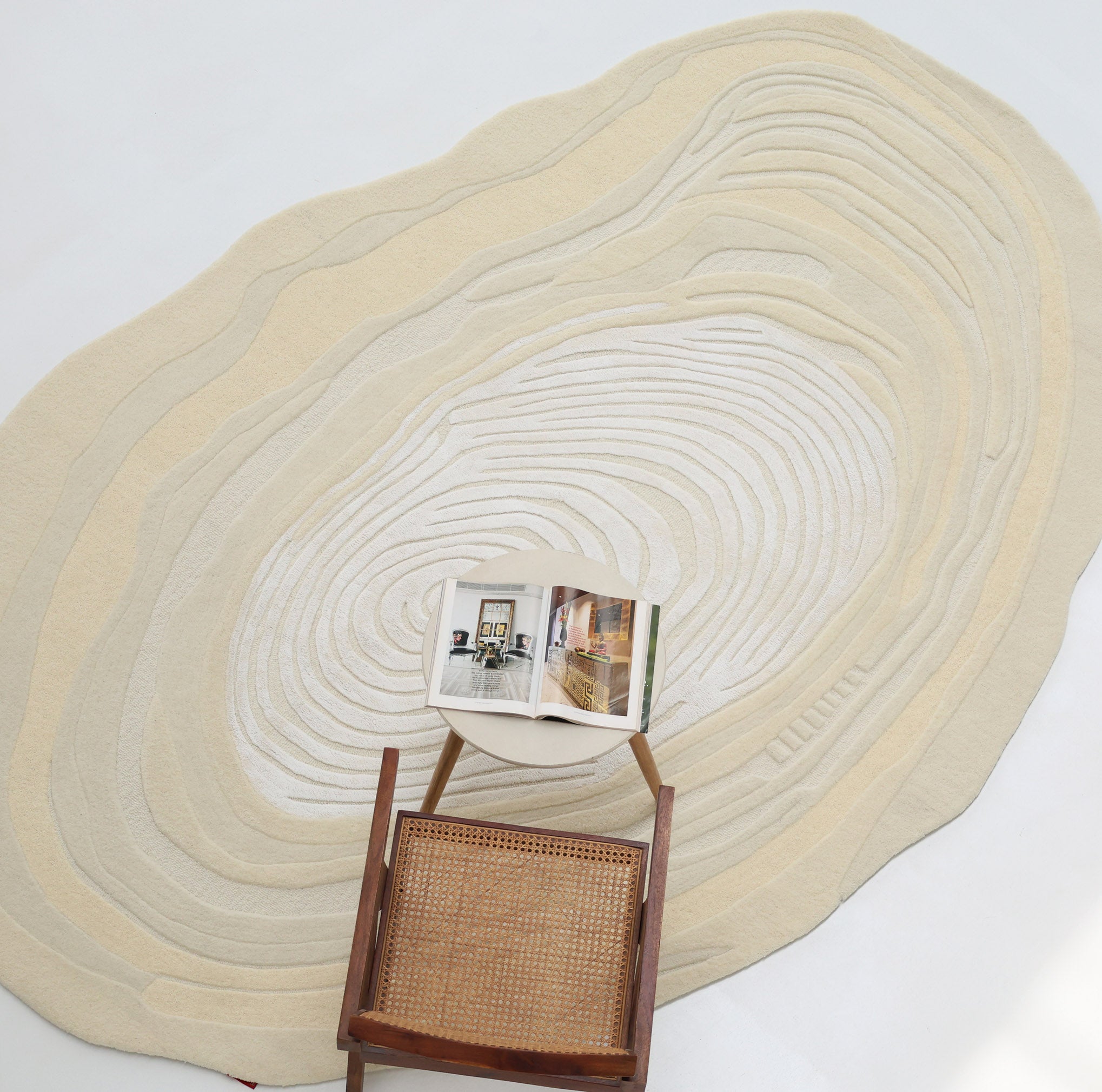 An Ivory Topographic Shaped Rug 200x300 cm by RAMSHA HOME lies on the floor. A wooden chair with a woven seat sits on the rug, with an open magazine resting on the chair.