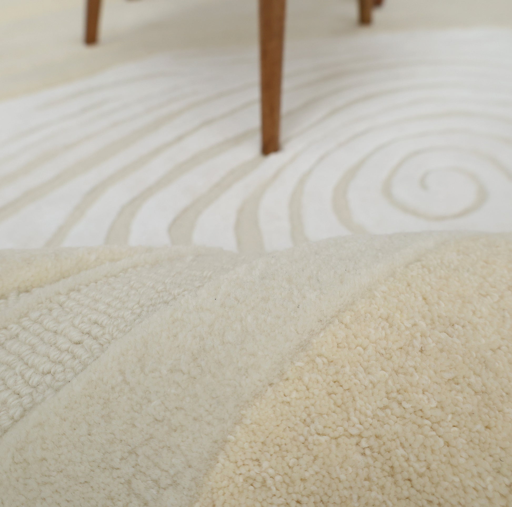 Close-up of the RAMSHA HOME Ivory Topographic Shaped Rug 200x300 cm (HTWV-192), showcasing its swirling, raised patterns and textured cream color, with wooden furniture legs visible in the background.