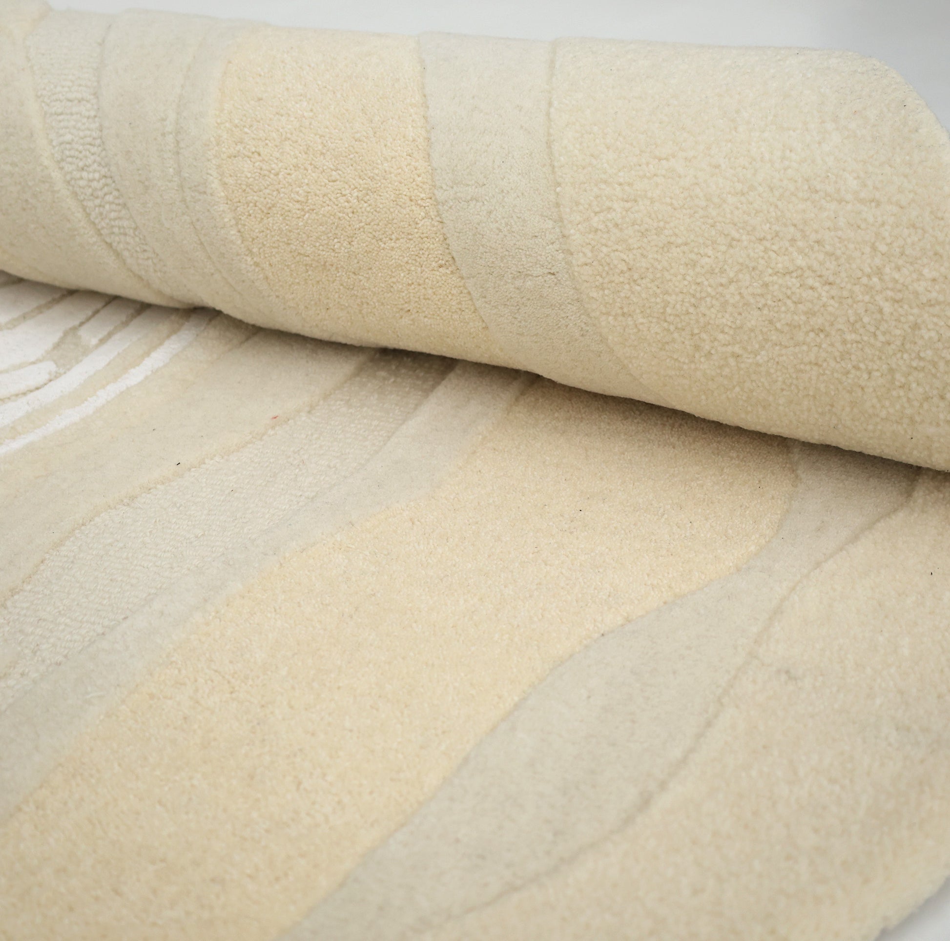 A close-up of the RAMSHA HOME Ivory Topographic Shaped Rug 200x300 cm (HTWV-192), partially rolled to highlight its plush surface and subtle cream and beige shades.