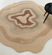 The RAMSHA HOME Luxury Abstract Contour Rug – Soft Textured Beige Accent Rug HTWV-194, featuring layered tan and brown patterns, is placed beside a black round table on a white floor.