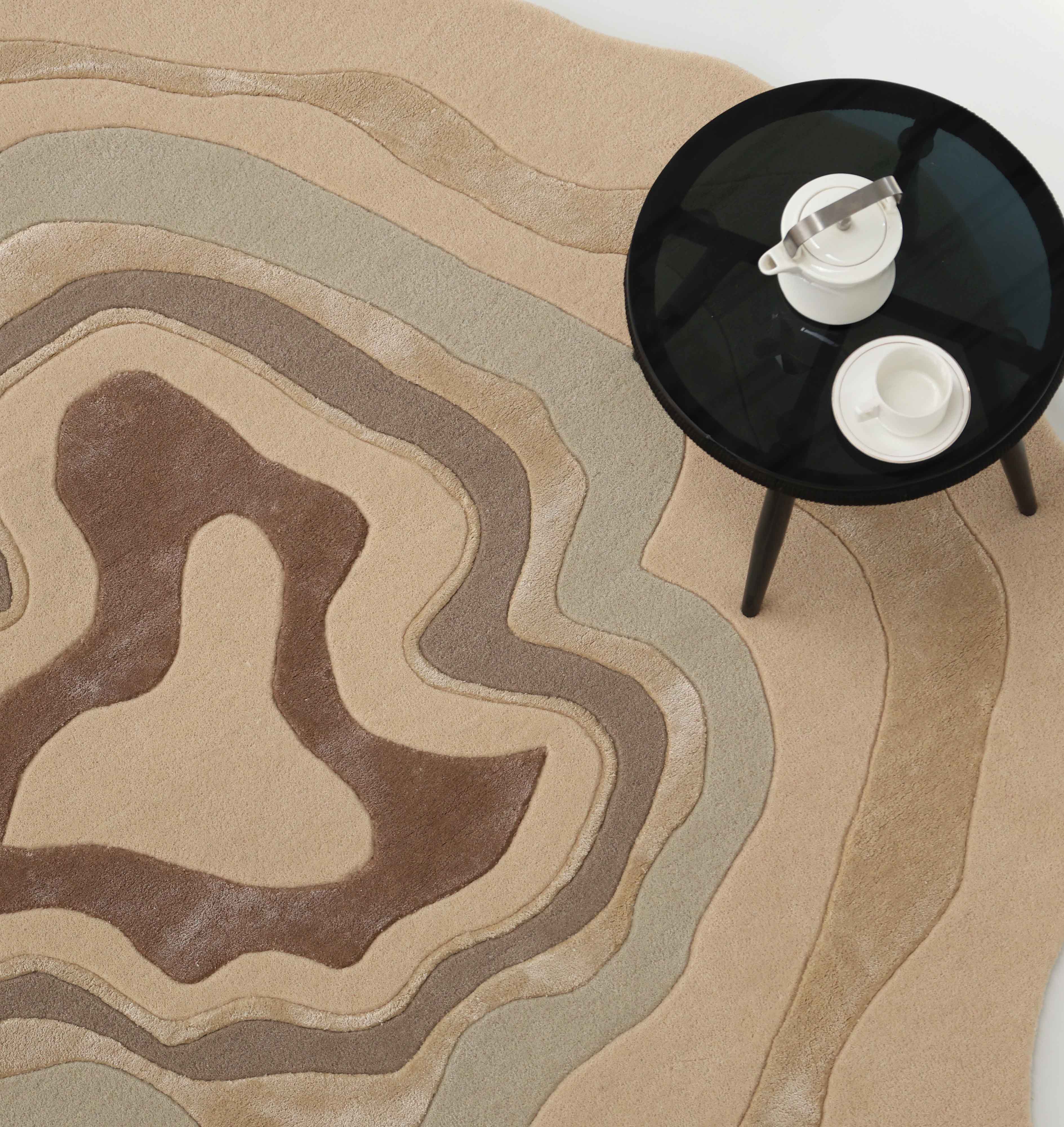 A modern round black table with a white teapot and cup sits on the RAMSHA HOME Luxury Abstract Contour Rug HTWV-194, a soft textured beige accent rug featuring wavy abstract patterns.