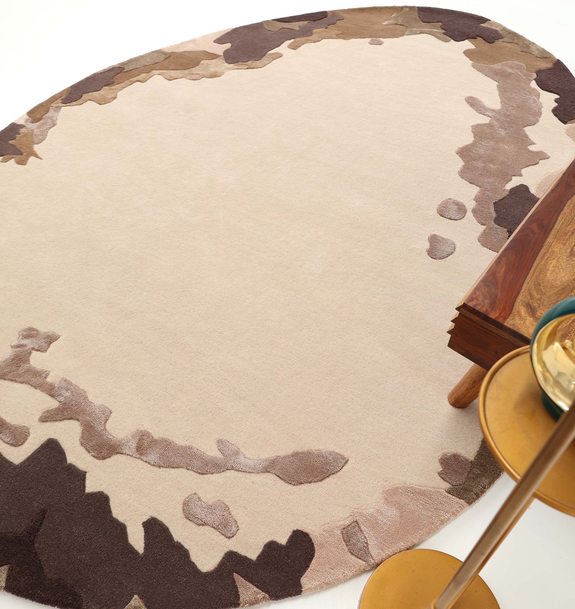 The RAMSHA HOME Terra Eclipse Oval Handmade Rug HTWV-195 features a beige center with brown, taupe, and tan borders, adding warmth beside wooden tables and gold round side tables on a white floor.