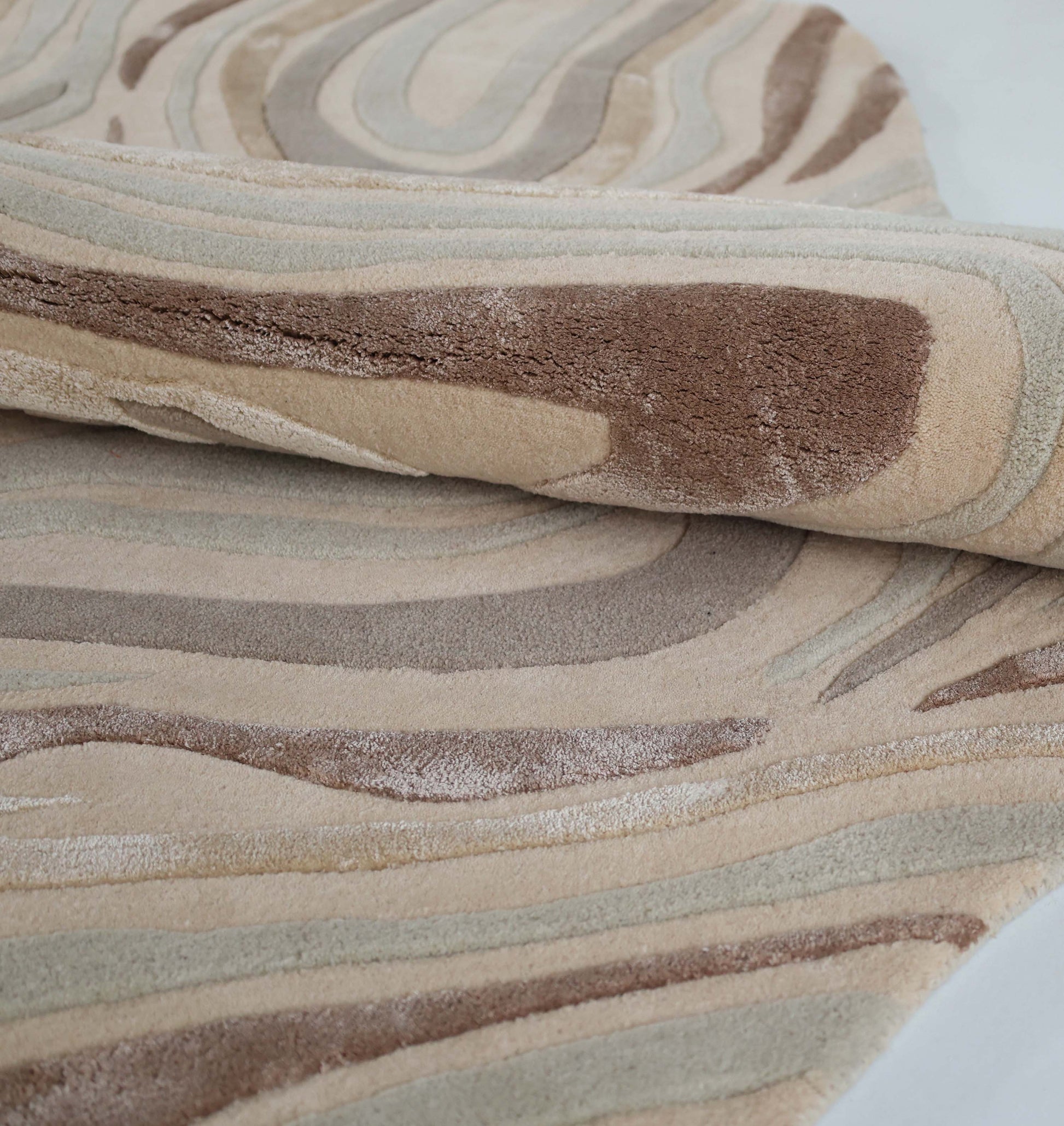 A close-up of the Desginer Freeform Handmade Rug HTWV-196 by RAMSHA HOME shows its rolled, textured surface with wavy abstract patterns in beige, brown, and tan. The plush, varied pile adds softness—perfect for a modern interior setting.