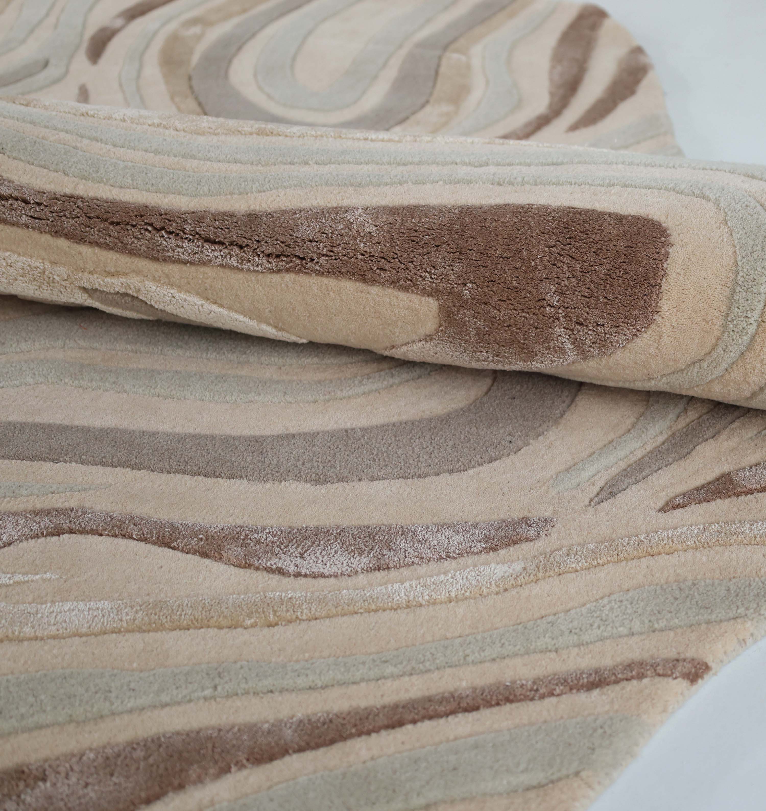 A close-up of the Desginer Freeform Handmade Rug HTWV-196 by RAMSHA HOME shows its rolled, textured surface with wavy abstract patterns in beige, brown, and tan. The plush, varied pile adds softness—perfect for a modern interior setting.