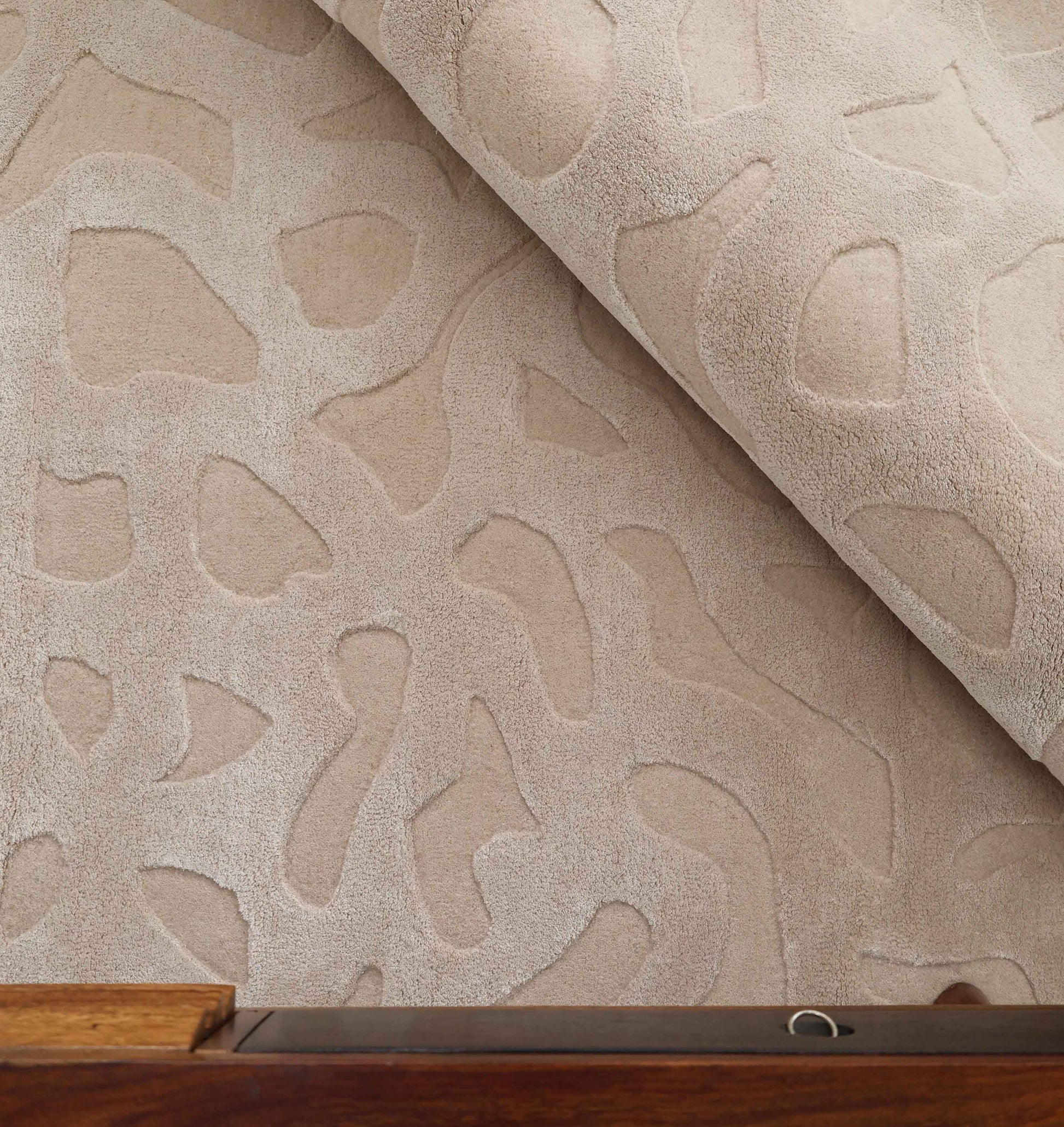 The RAMSHA HOME Rectangle Modern Handmade Rug 200x300 CM HTWV-197 features a beige, hand-woven abstract design with raised textures, partially rolled on a wooden surface to highlight its plush, soft material.