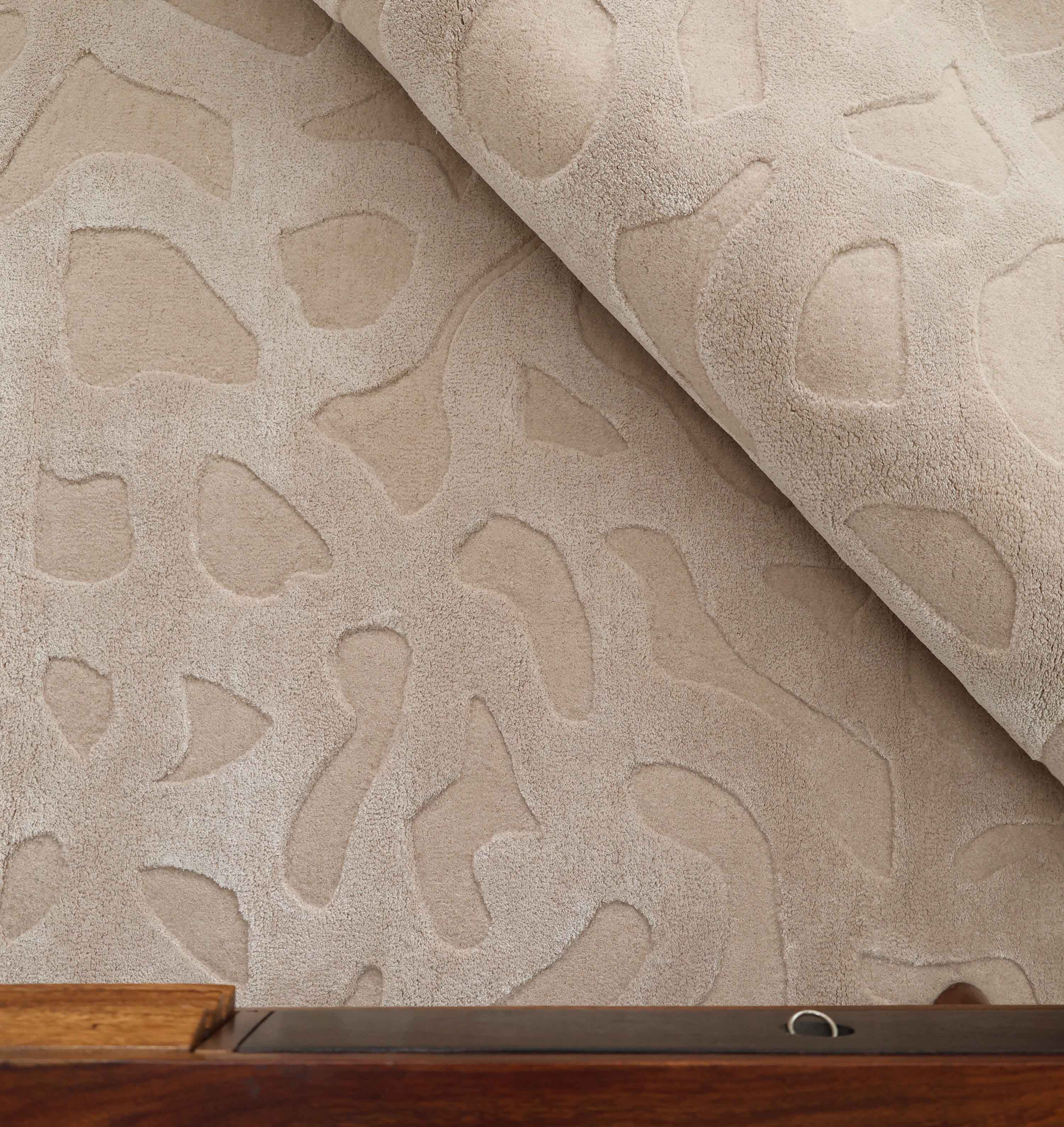 The RAMSHA HOME Rectangle Modern Handmade Rug 200x300 CM HTWV-197 features a beige, hand-woven abstract design with raised textures, partially rolled on a wooden surface to highlight its plush, soft material.