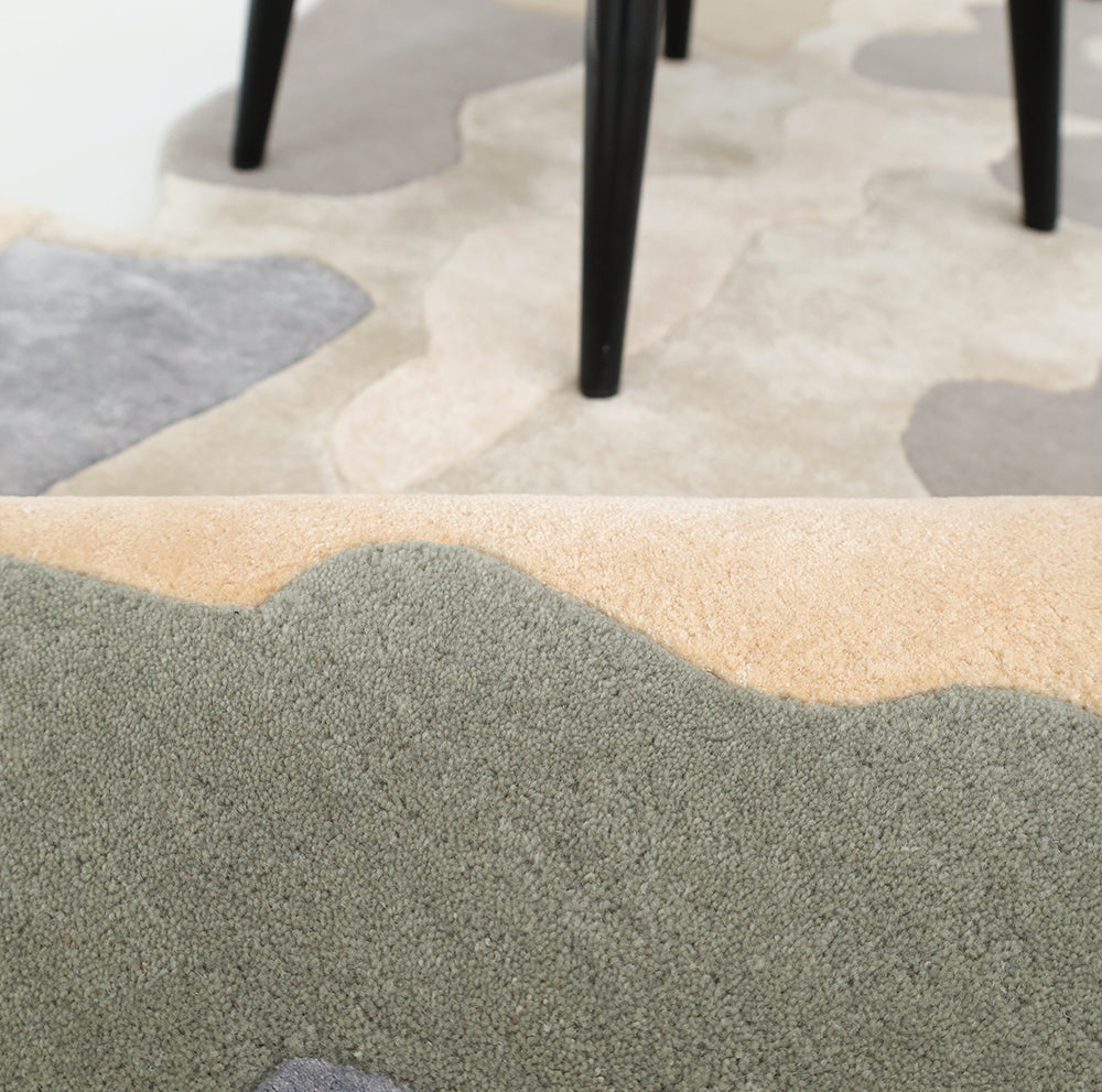 Close-up of the RAMSHA HOME Contemporary Flow Area Handmade Rug HTWV-199, featuring a textured, abstract pattern in beige, gray, and green. Black chair legs highlight the rug’s modern style in this interior setting.