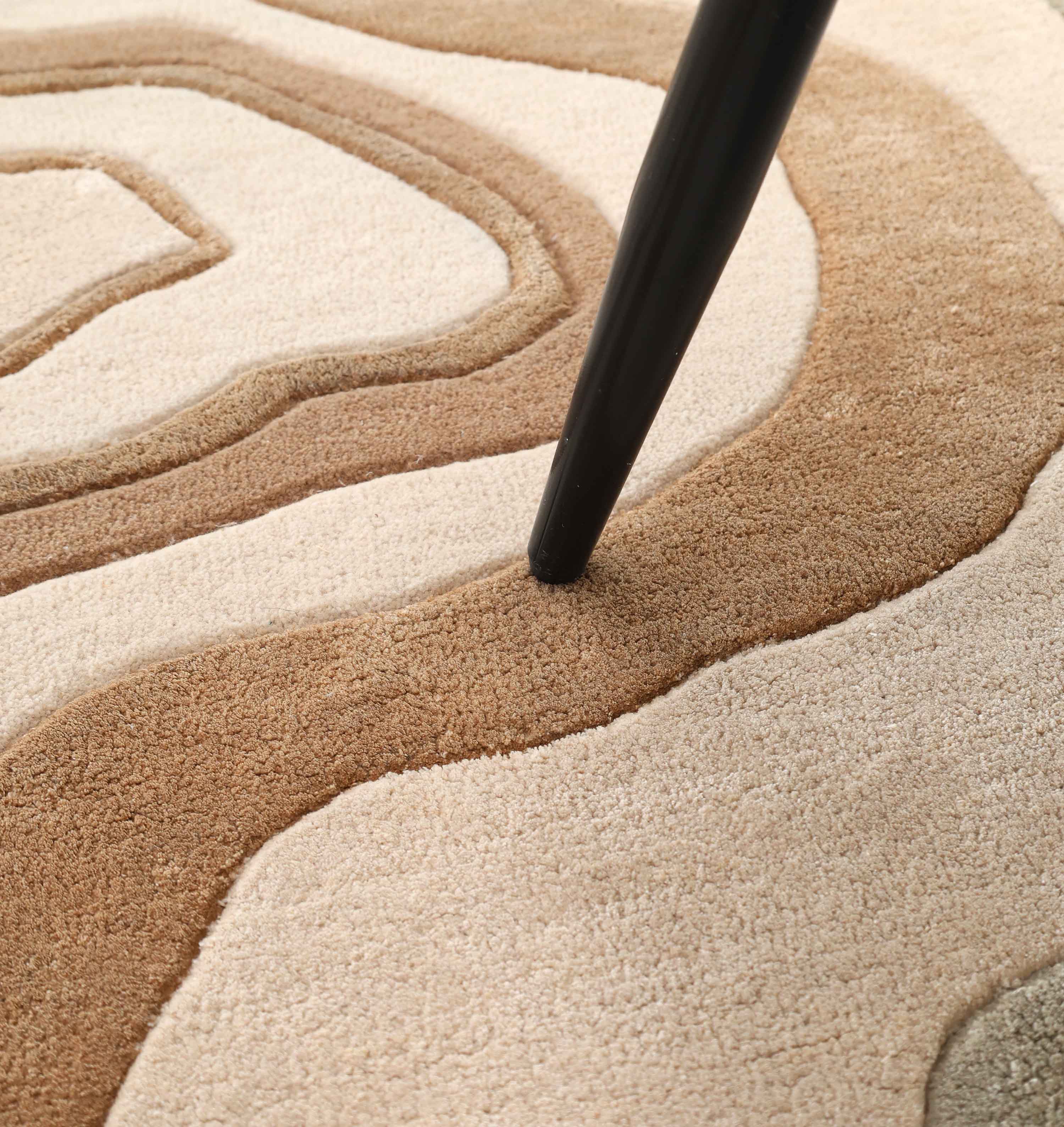 A black tapered furniture leg rests on the RAMSHA HOME Designer Freeform Handmade Rug HTWV-200, featuring a textured, wavy pattern in beige, tan, and brown.